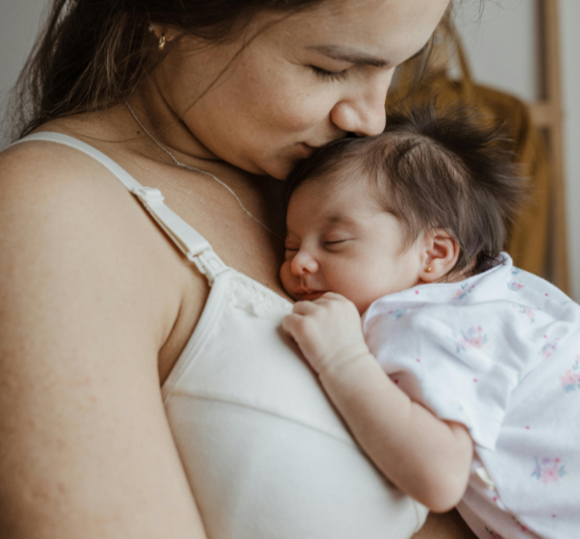 A woman holding a sleeping baby close to her chest, with her face gently touching the baby's head.
