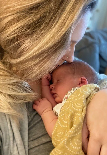 A woman holding a sleeping newborn baby close to her face, both in a tender moment.