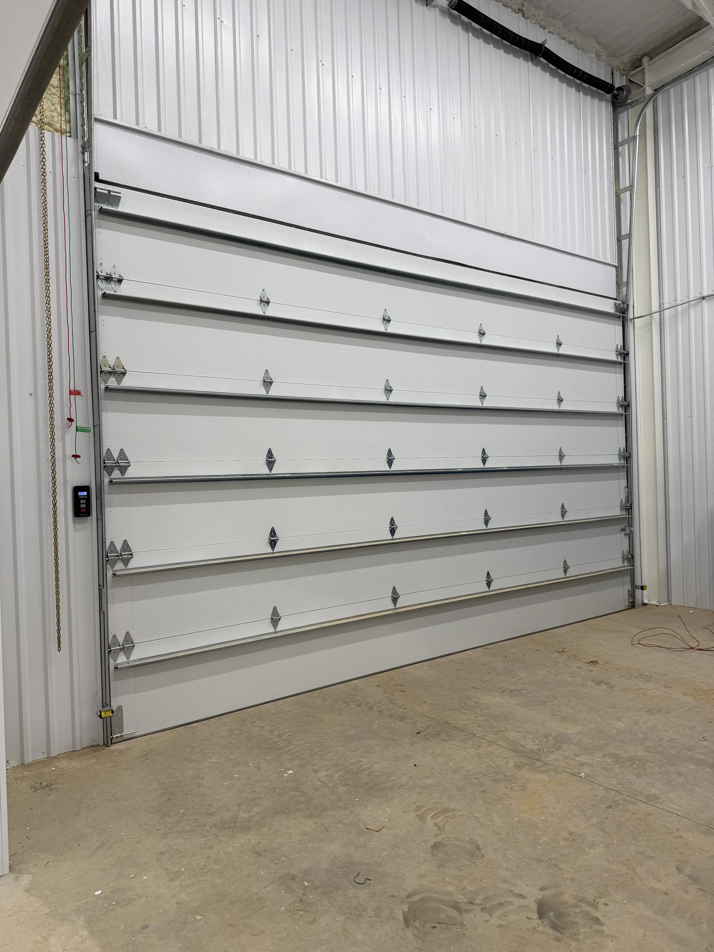 A large white industrial roll-up garage door installed in a building with unfinished concrete floor and walls.