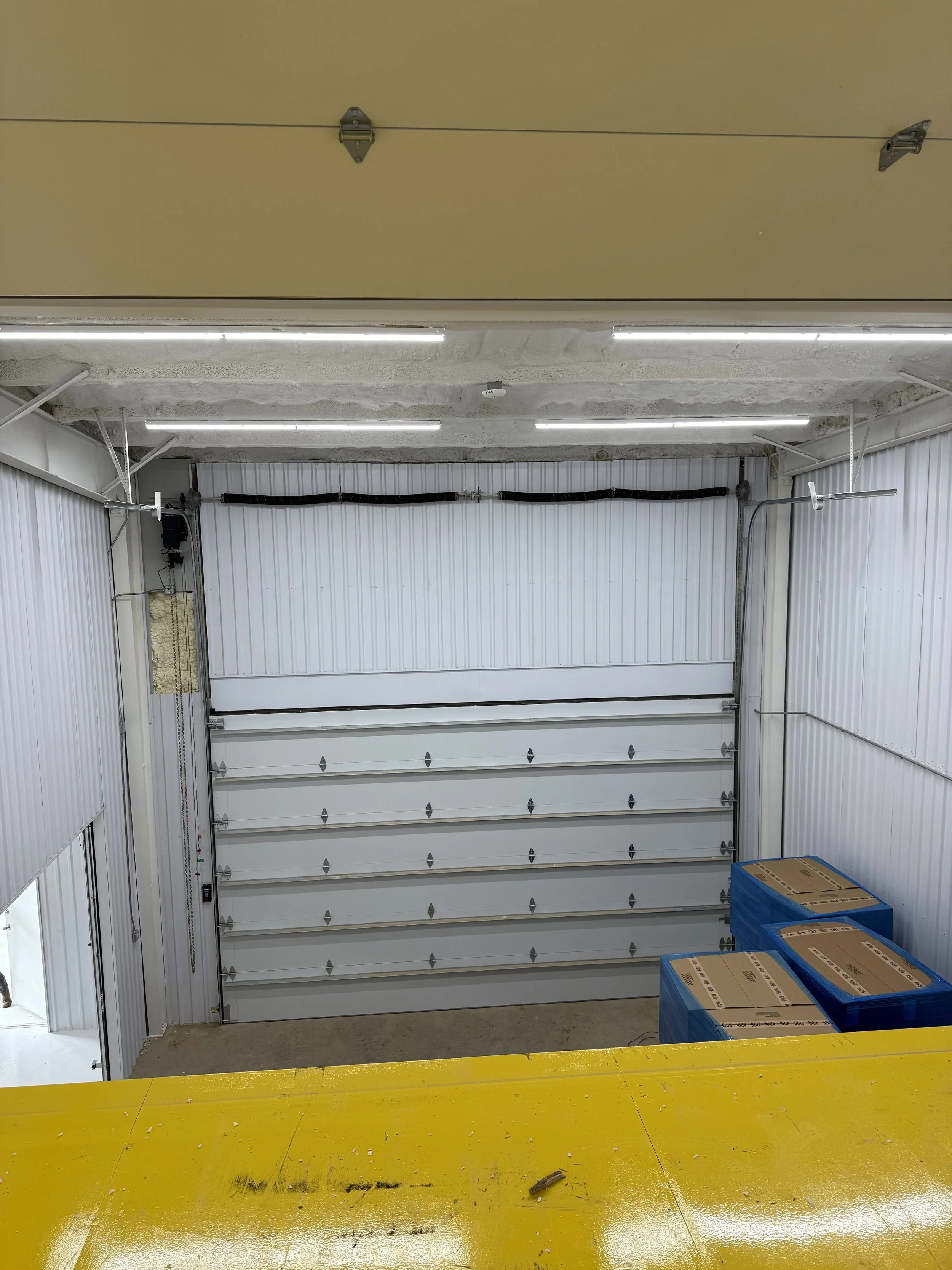 View of an industrial garage door with a yellow painted concrete floor and boxes stored on the side.