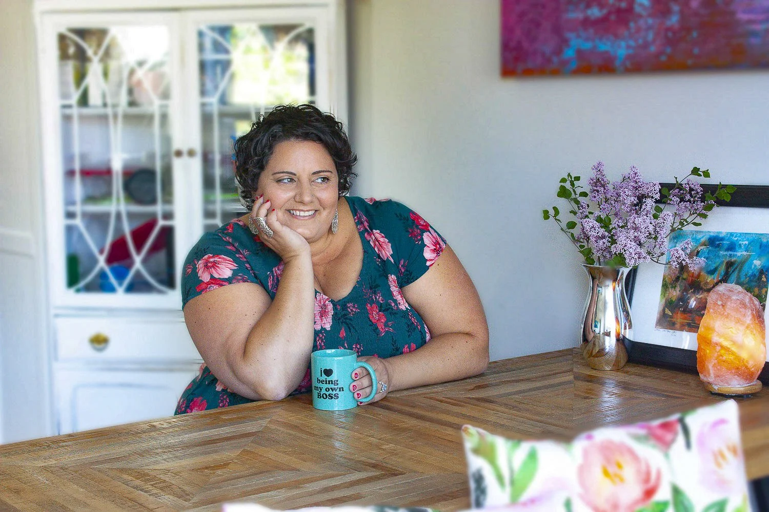 Sophia Apostol, founder of Fat Joy Creation Lab, wearing a blue dress with pink flowers and resting her face on her hand