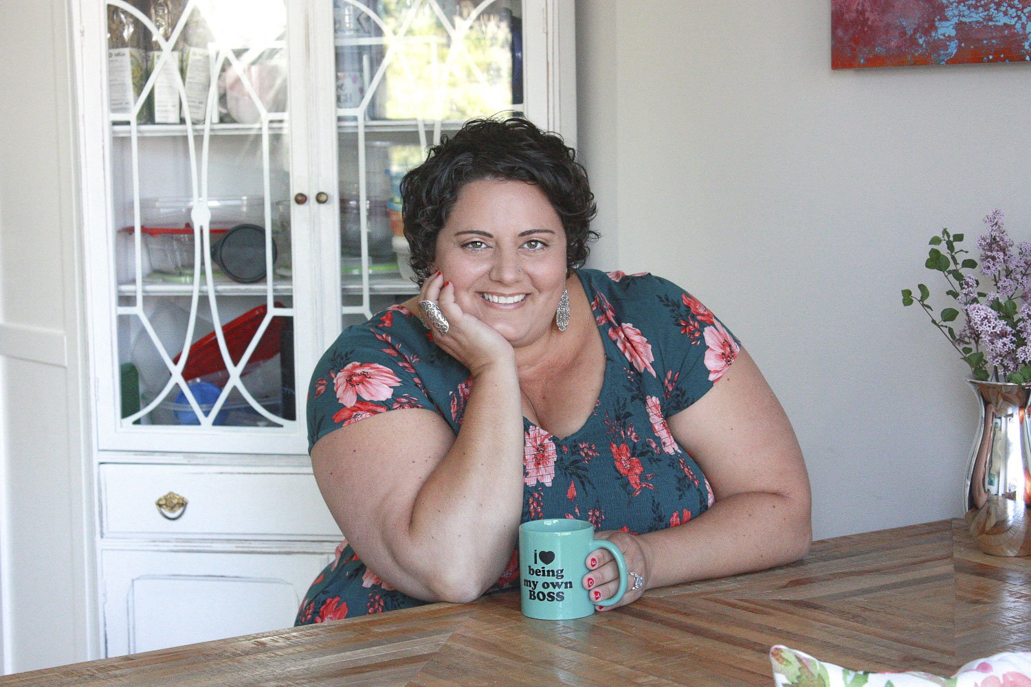 A white plus-size woman with light brown hair and wearing a vibrant teal dress, joyfully stretches dough in a bright kitchen. The scene embodies creativity, community, and fat liberation, celebrating body positivity and joyful expression.
