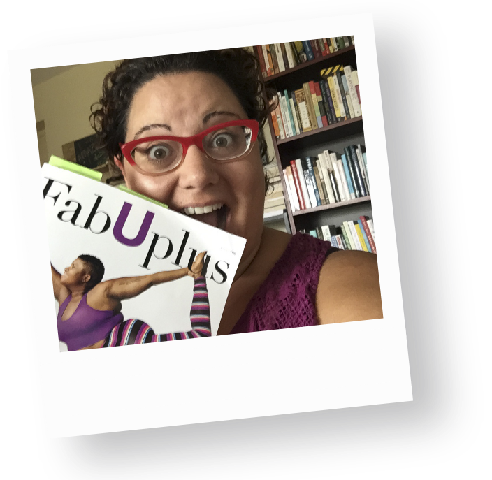 Sophia Apostol, a plus-size white woman and the founder of Fat Joy Creation Lab, with curly hair and vibrant red glasses holds up a magazine, showcasing body positivity. A colorful bookshelf filled with diverse literature is behind.