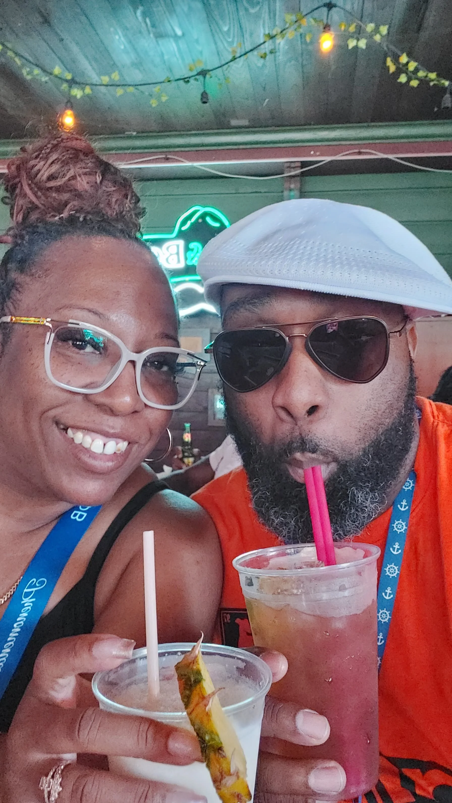 A smiling woman with glasses and a woman with a white hat and dark sunglasses enjoying drinks at a bar.