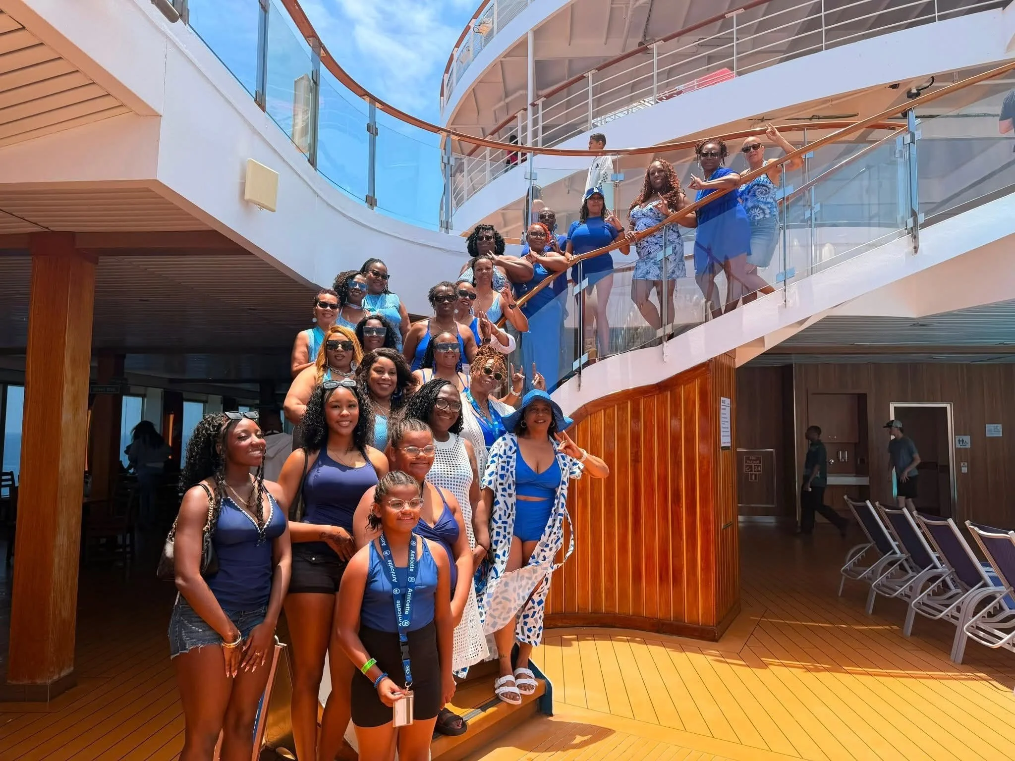 A group of women and young girls in blue outfits posing on the stairs of a ship's deck under a blue sky.