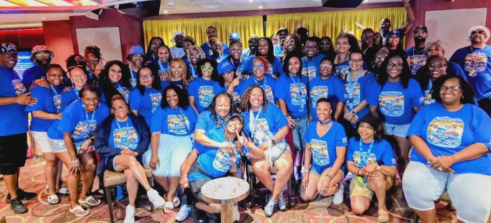 Group of people smiling and posing for a photo in a room, all wearing matching blue T-shirts with a colorful graphic design.