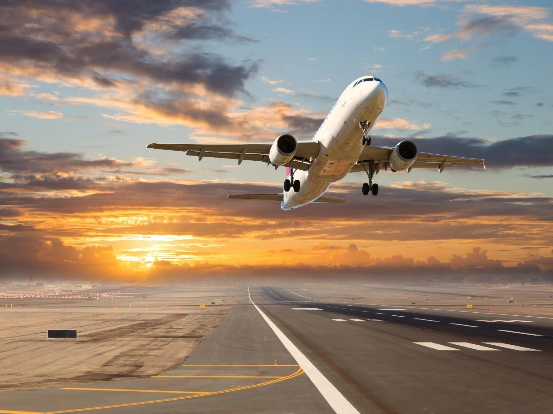 An airplane taking off from a runway during sunset with dramatic clouds in the sky.