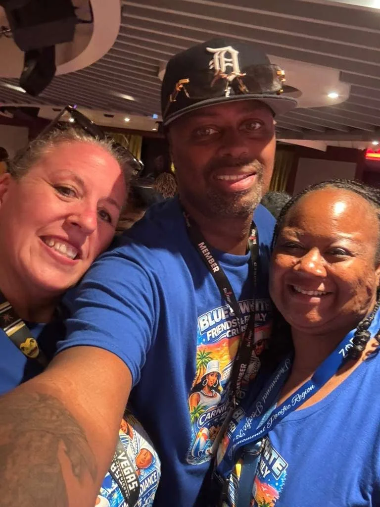 Three people taking a selfie together at an event, all wearing blue shirts with event logos and lanyards.