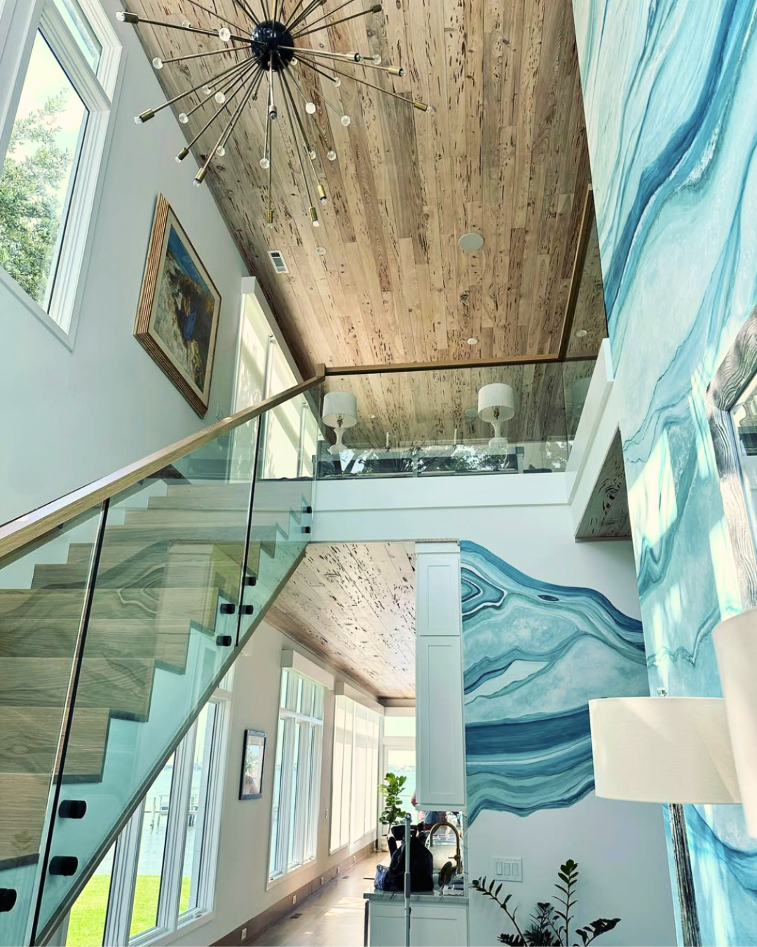 Interior view of a modern, multi-level home with large windows, a wooden ceiling, and a blue and white marbled accent wall.