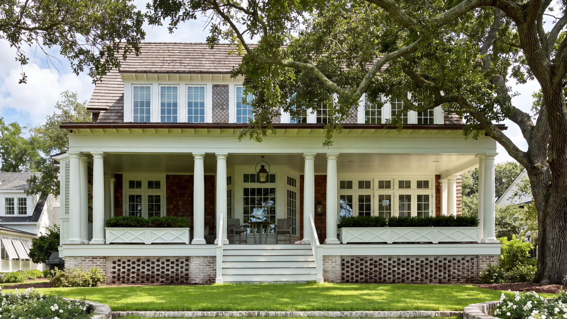 Front view of a large two-story house with white columns, porch, and multiple windows, surrounded by green grass and trees.