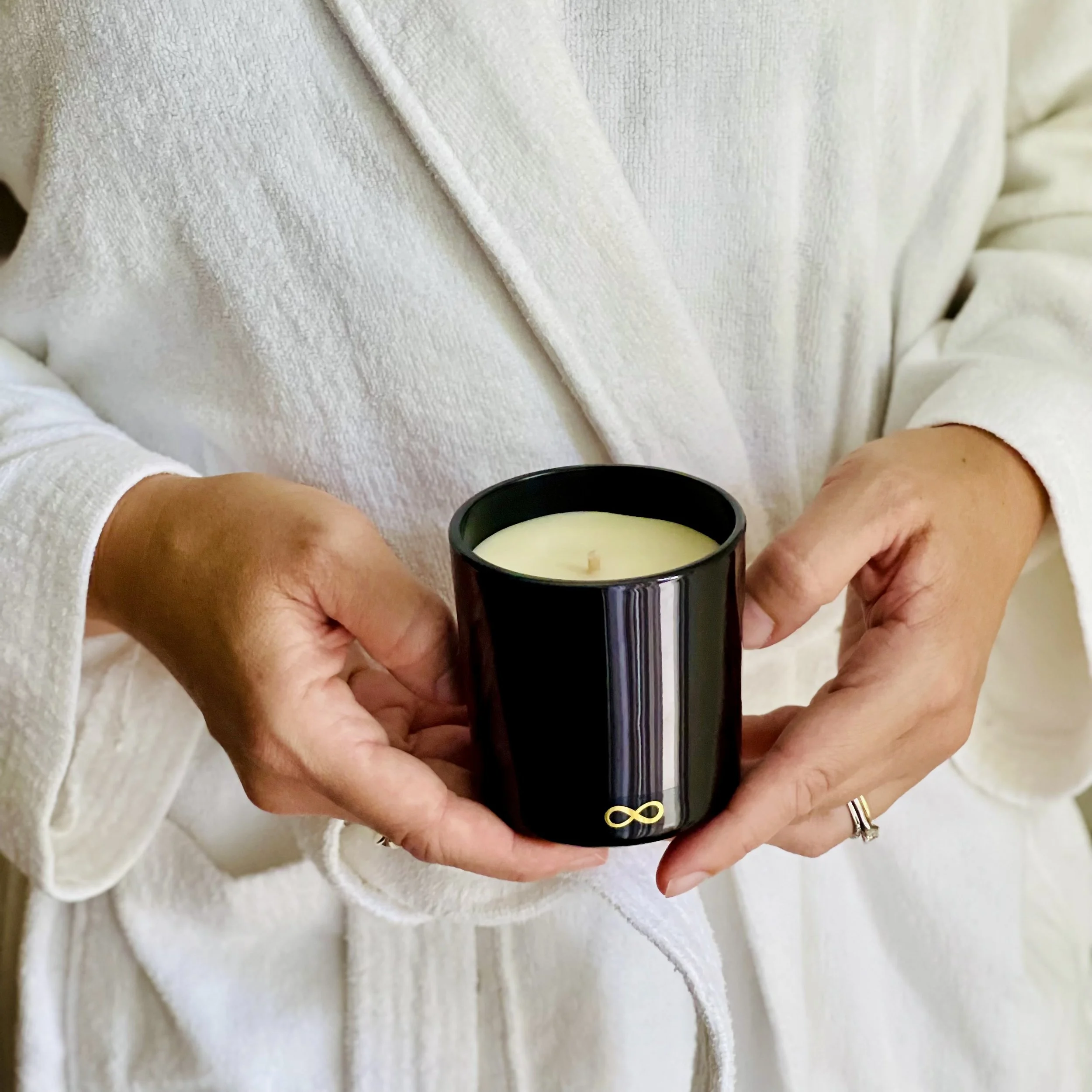Close-up of a person holding a black elegant botanical candle on a spa robe.