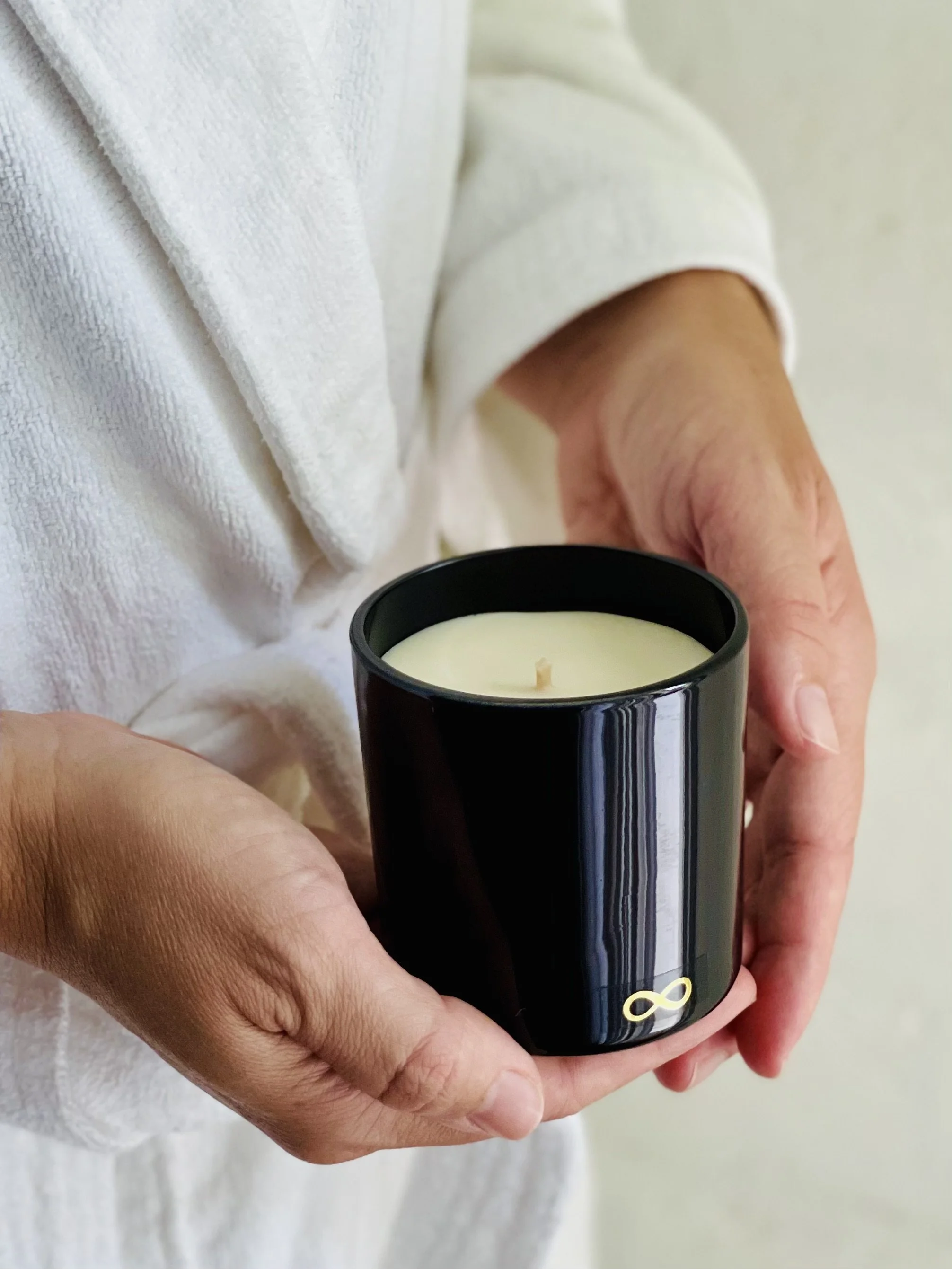 A person holding a black botanical candle with a gold infinity symbol on it.