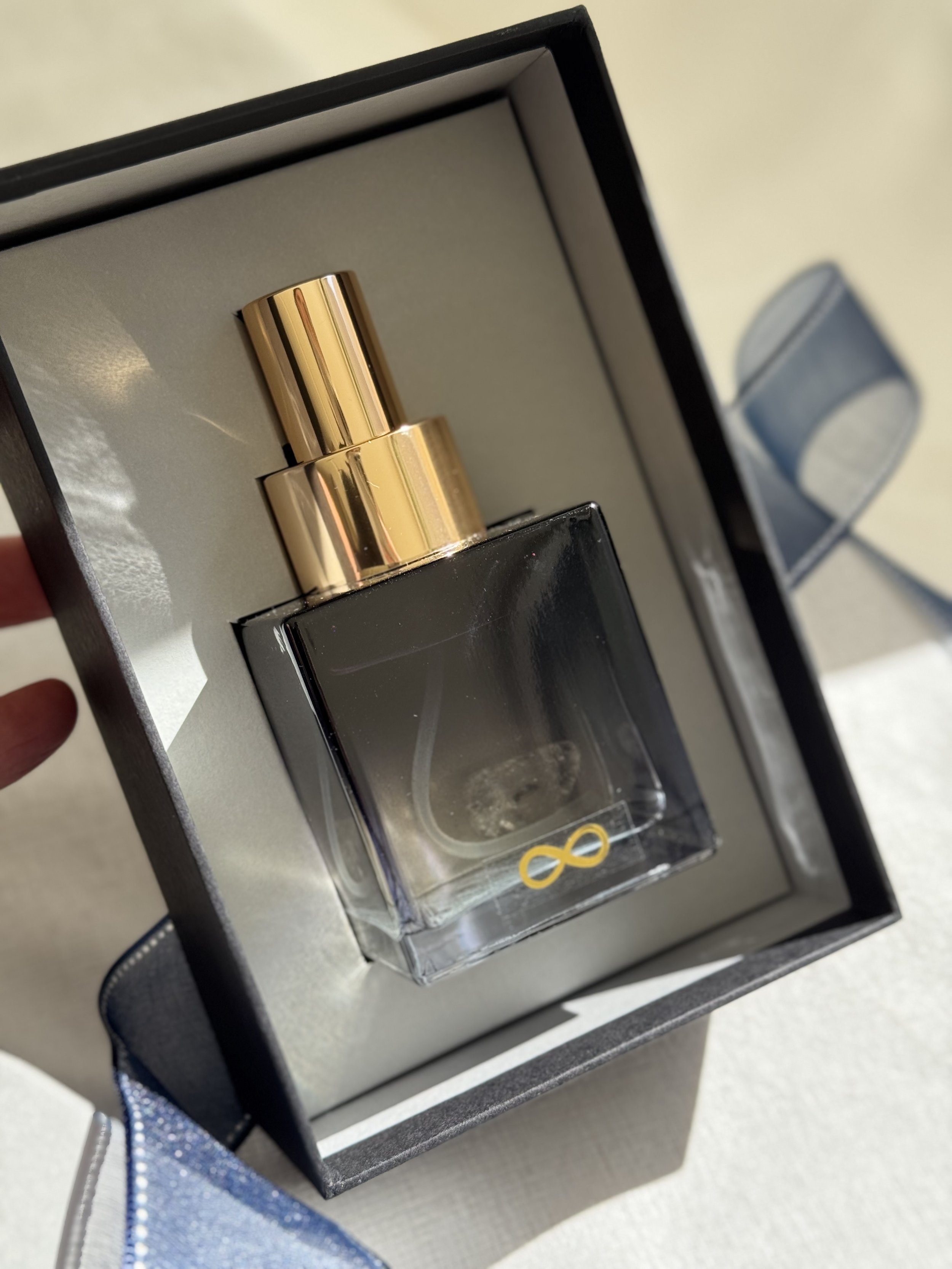Close-up of a black gift box containing a Voyde Bespoke perfume or cologne with a reflective surface, with a golden infinity symbol on it.
