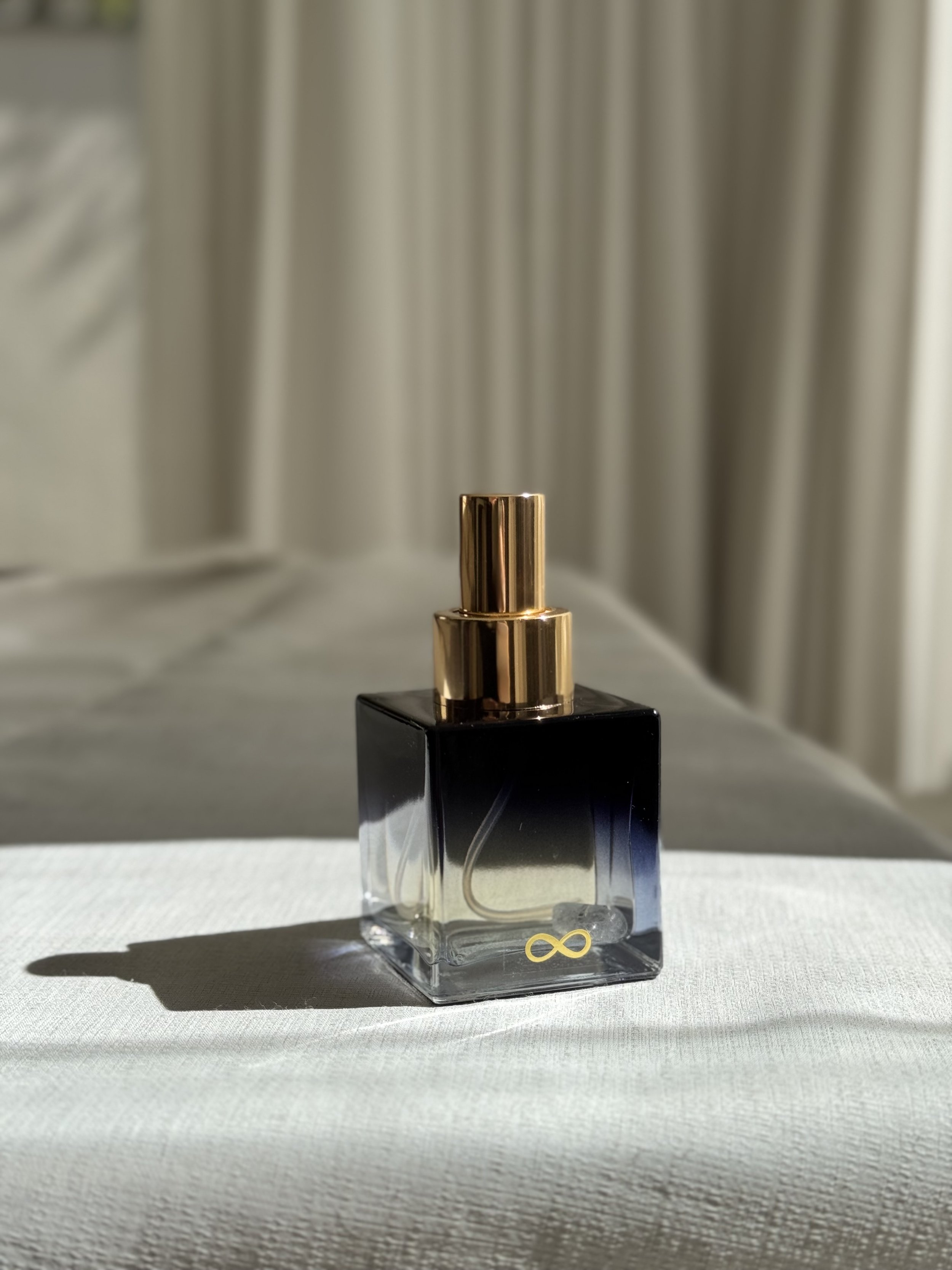 A Voyde Bespoke Atelier perfume bottle with a blue and gold color scheme, placed on a white surface with a curtain in the background.