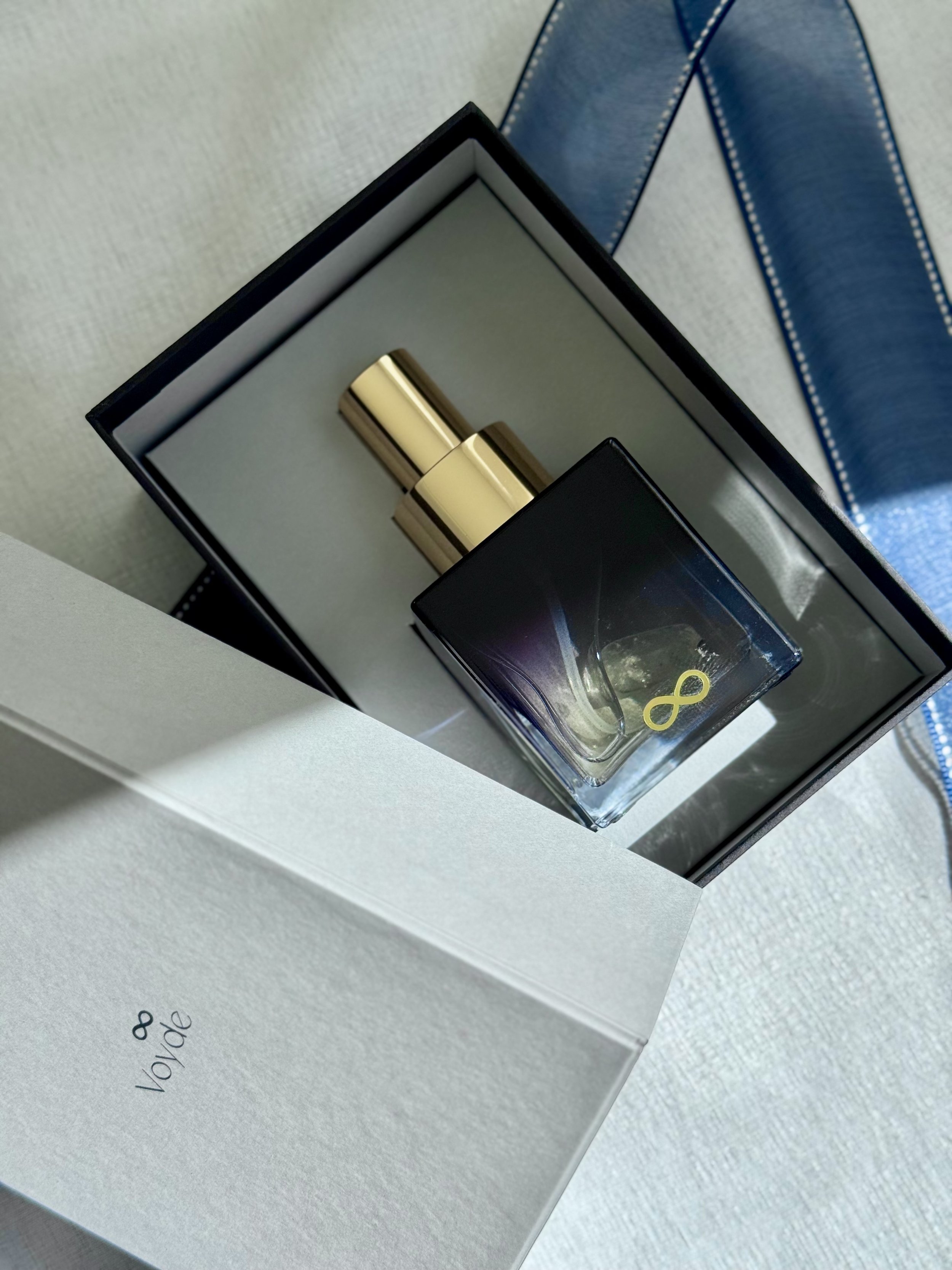 Close-up of a boxed Voyde Bespoke perfume or cologne with a gold bottle, alongside packaging and a reflective surface.