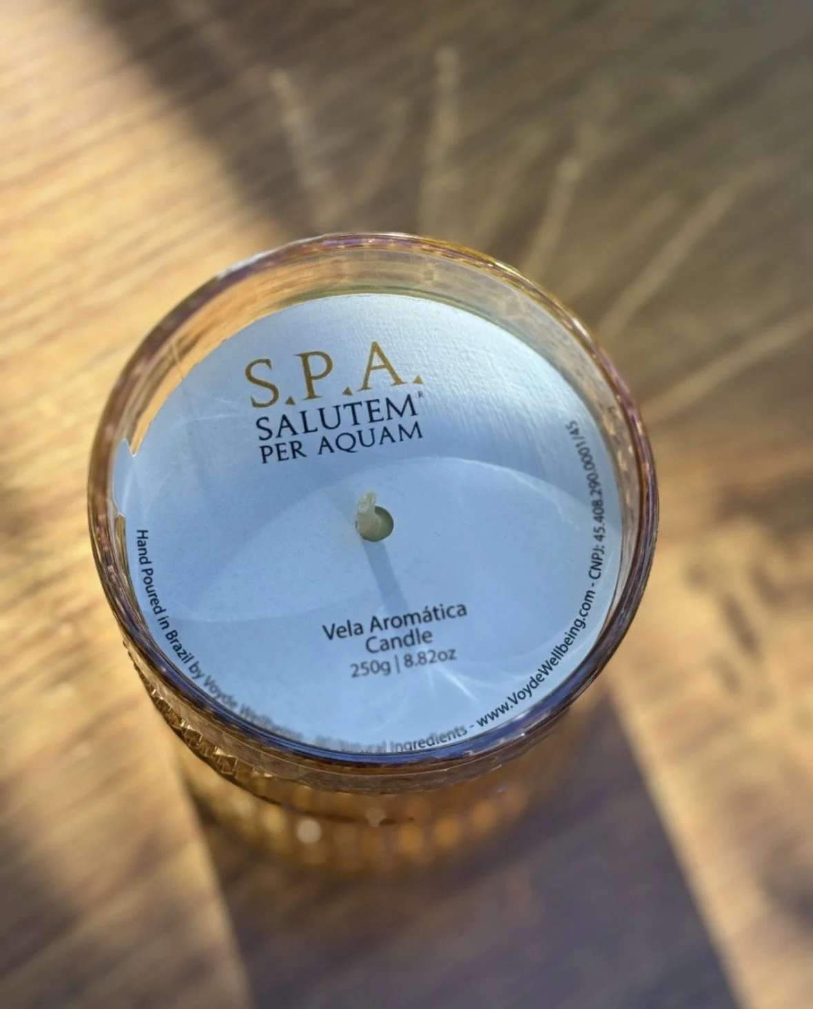 Top view of a bespoke candle jar labeled 'S.P.A. Salutem Per Aquam Vela Aromática Candle' on a wooden surface. By Voyde Wellbeing Signature Scenting