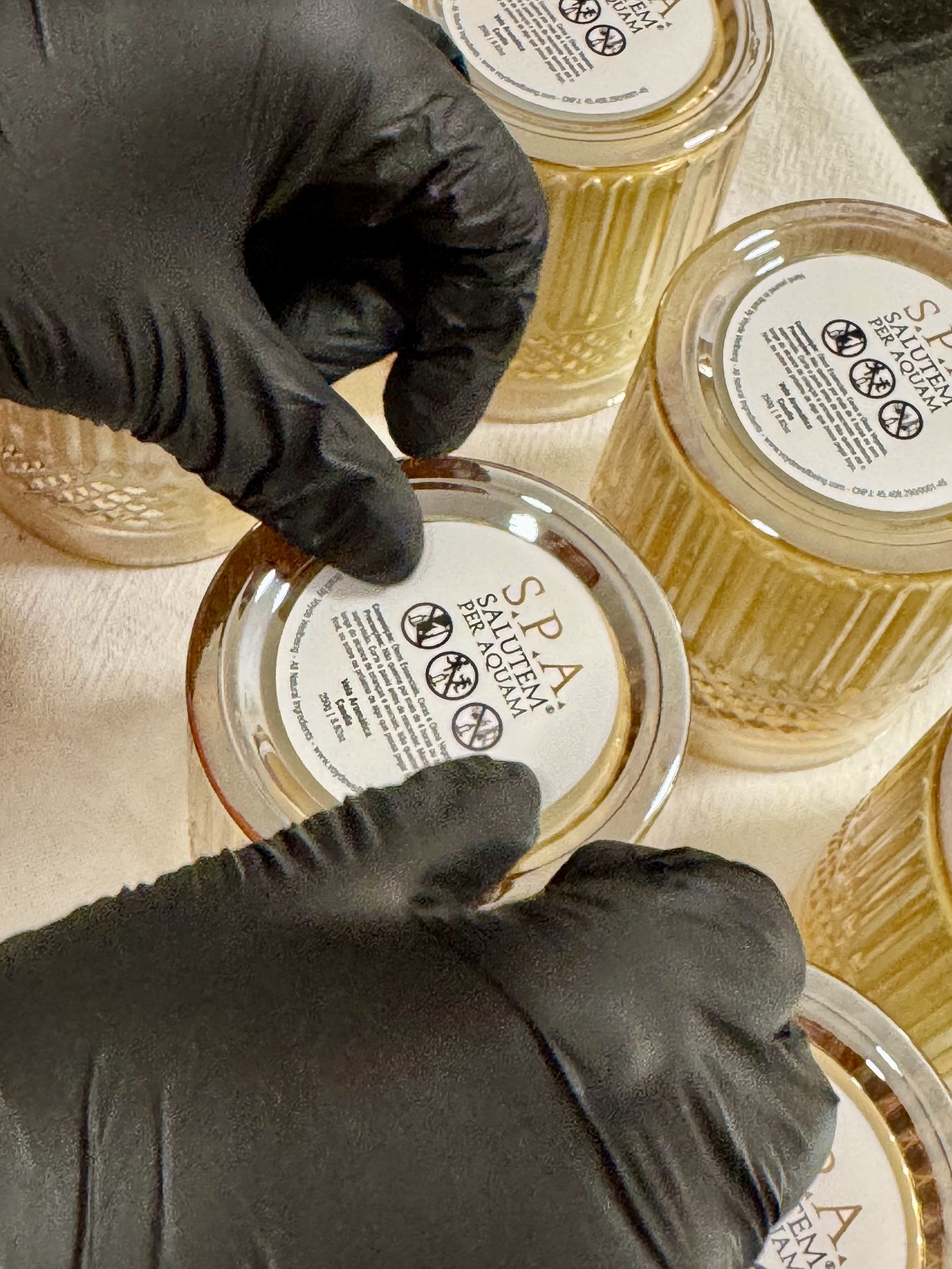 Close-up of a person's gloved hand producing and labeling bespoke candles for a business spa labeled 'Salute Per Aquam' by Voyde Wellbeing Signature Scenting for Business