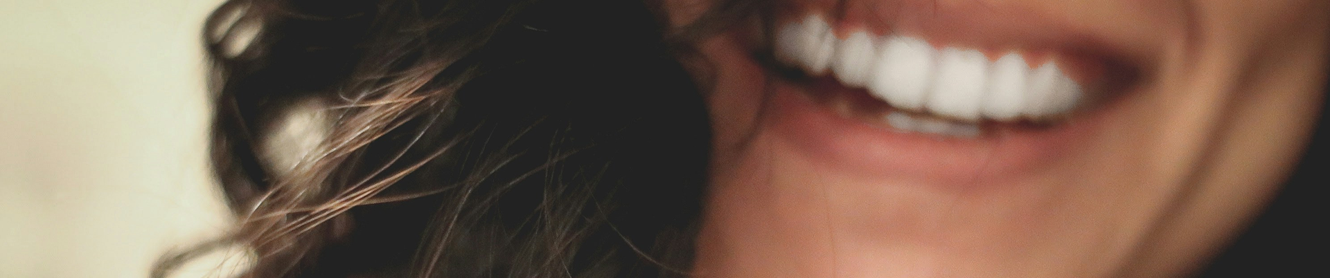 Close-up of a woman smiling, showing her teeth, with dark brown wavy hair partially covering her face.