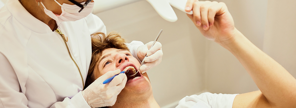 Dentist in white coat examining patient's open mouth in dental clinic.