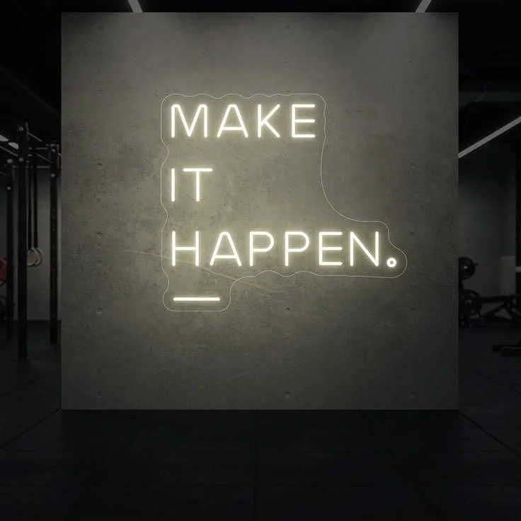 Neon sign on a wall that reads 'MAKE IT HAPPEN' with a period at the end.
