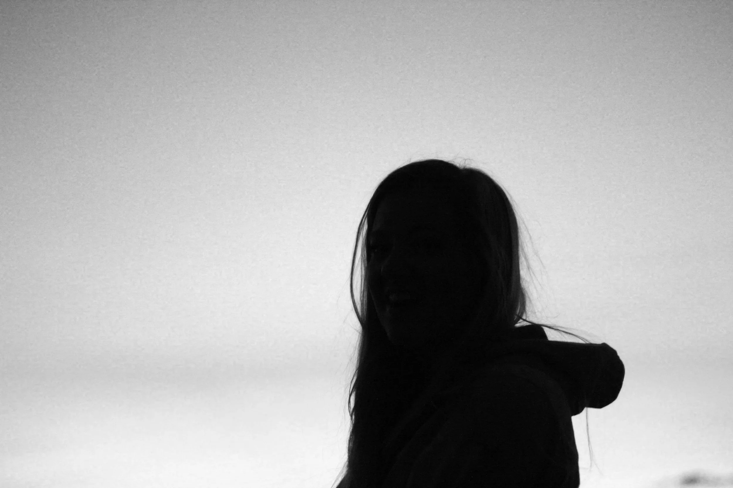Silhouette of a woman with long hair standing against a plain background.