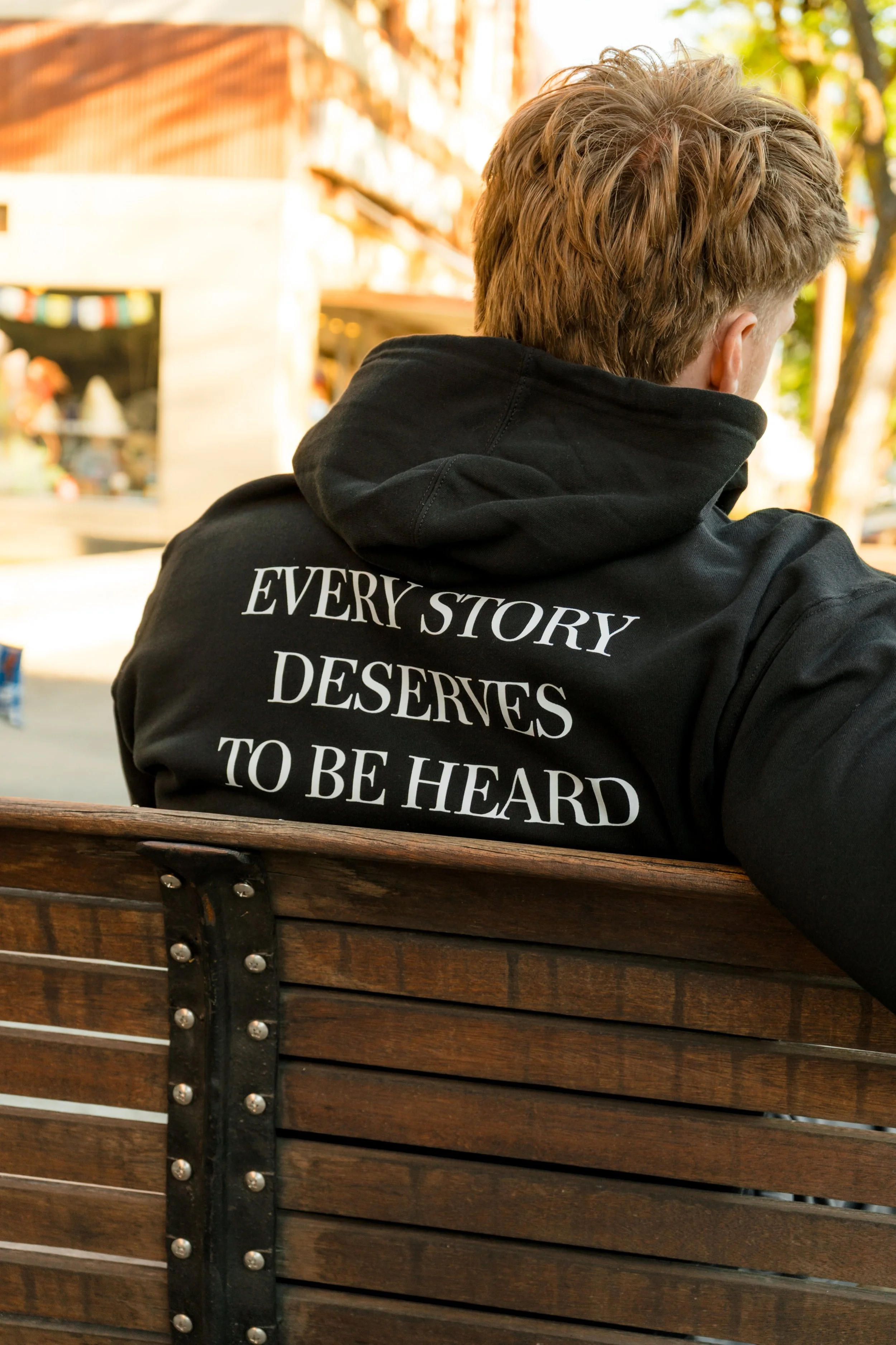 Person wearing a StandUp33 hoodie with the message "Every Story Deserves to Be Heard" while sitting outdoors.