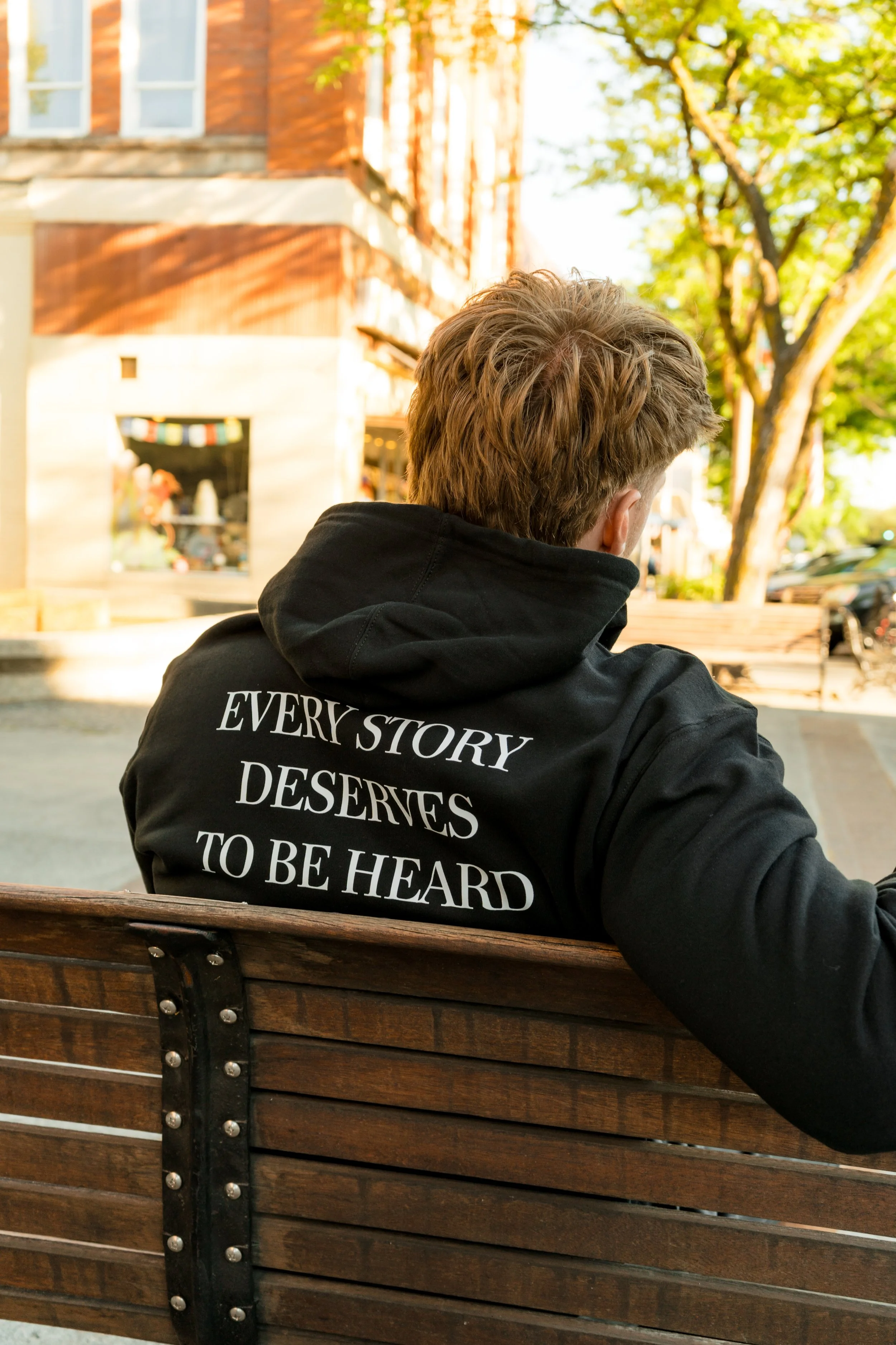 Back view of a person wearing a StandUp33 hoodie with the message "Every Story Deserves to Be Heard."