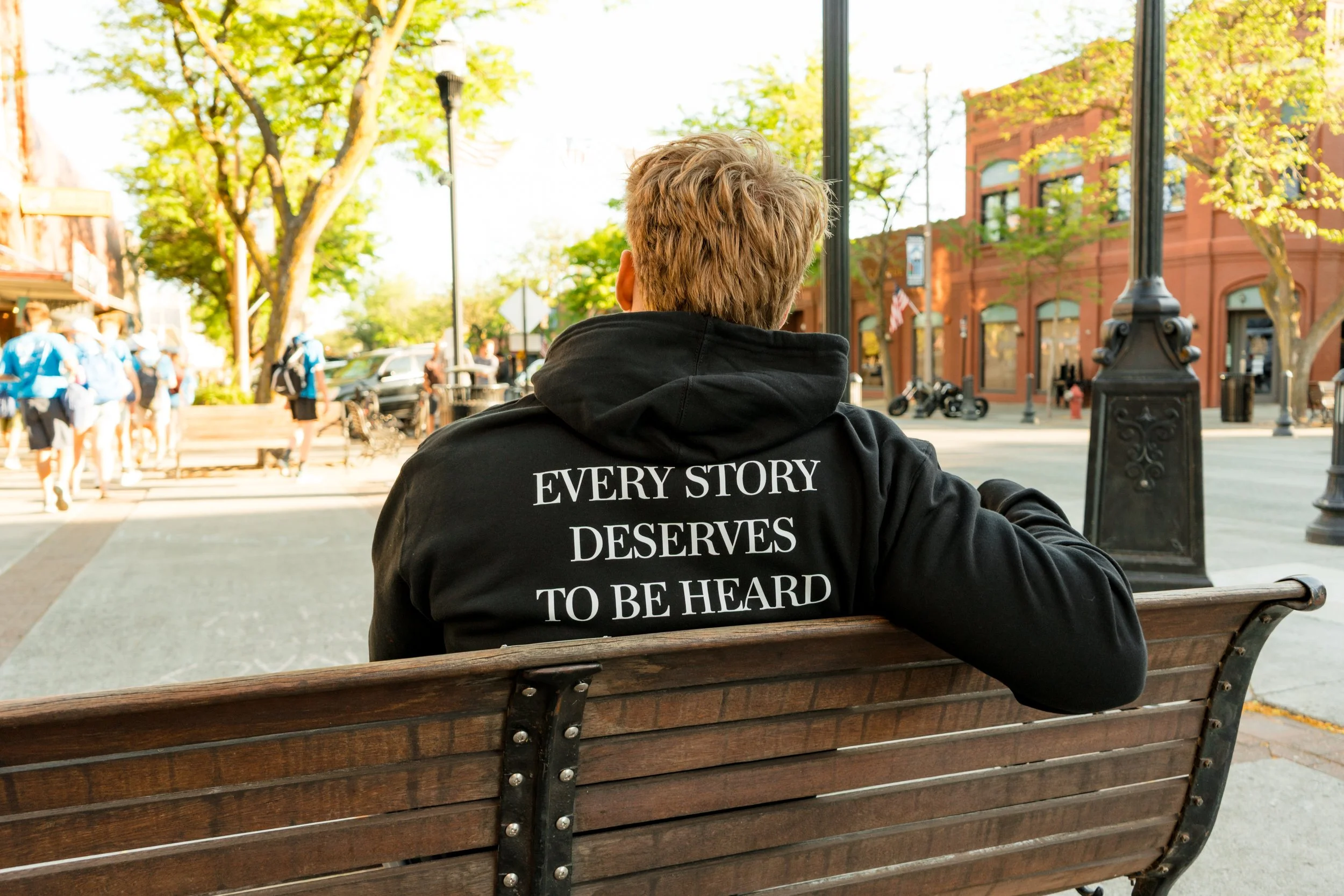 Back view of a person wearing a StandUp33 hoodie with the message "Every Story Deserves to Be Heard."