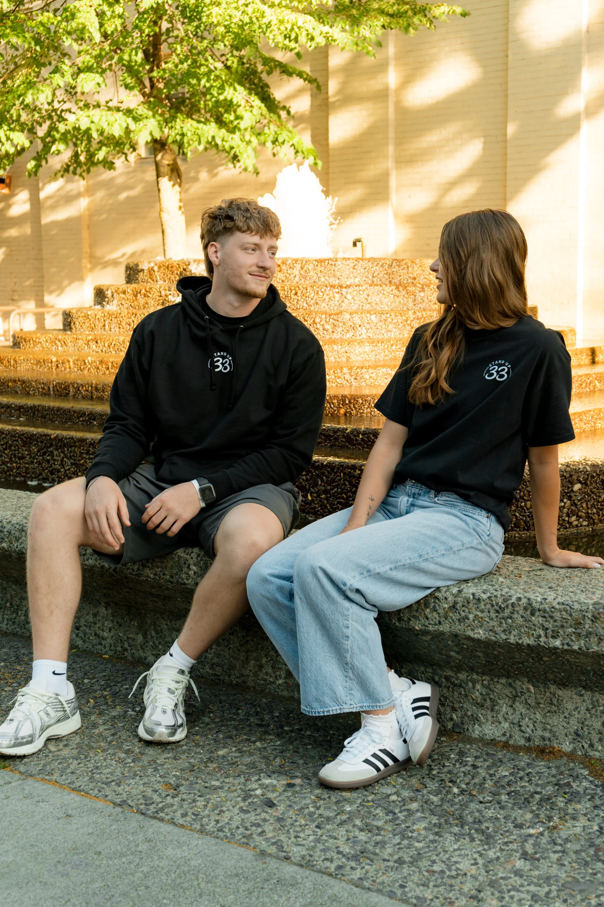 Two people wearing StandUp33 hoodies while sitting together and talking outdoors.