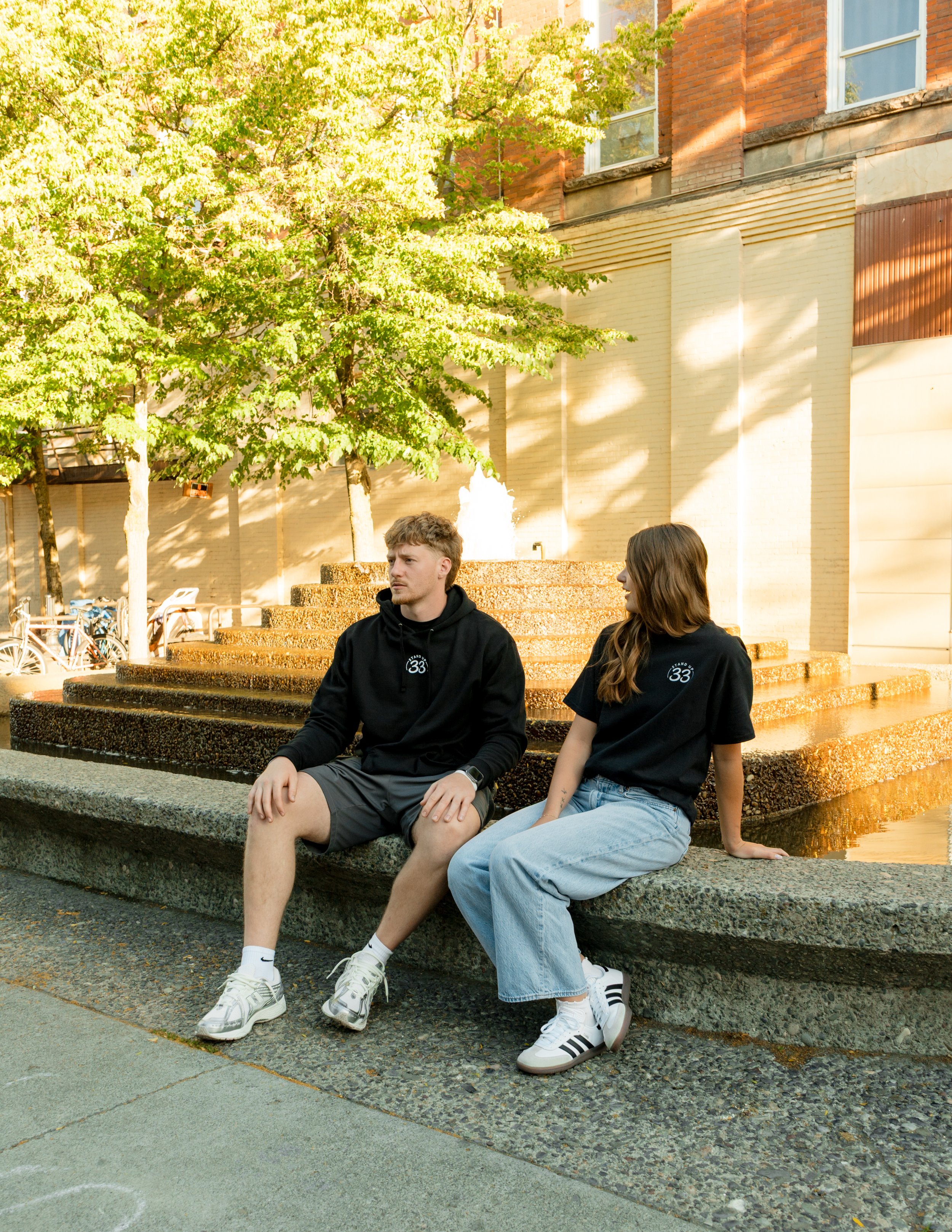Two people wearing StandUp33 awareness apparel while sitting near a fountain.