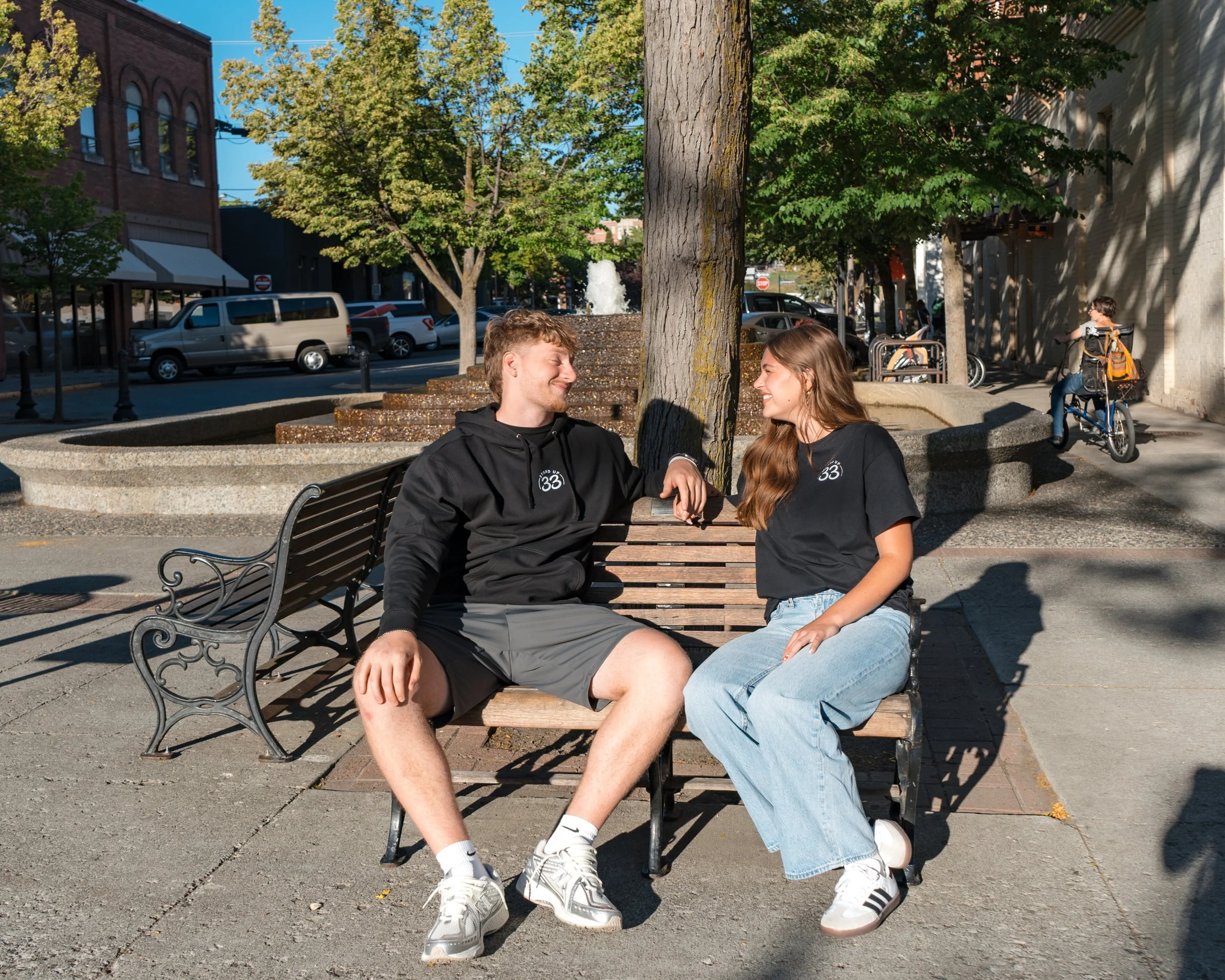 Person wearing a StandUp33 hoodie while sitting on a park bench outdoors.
