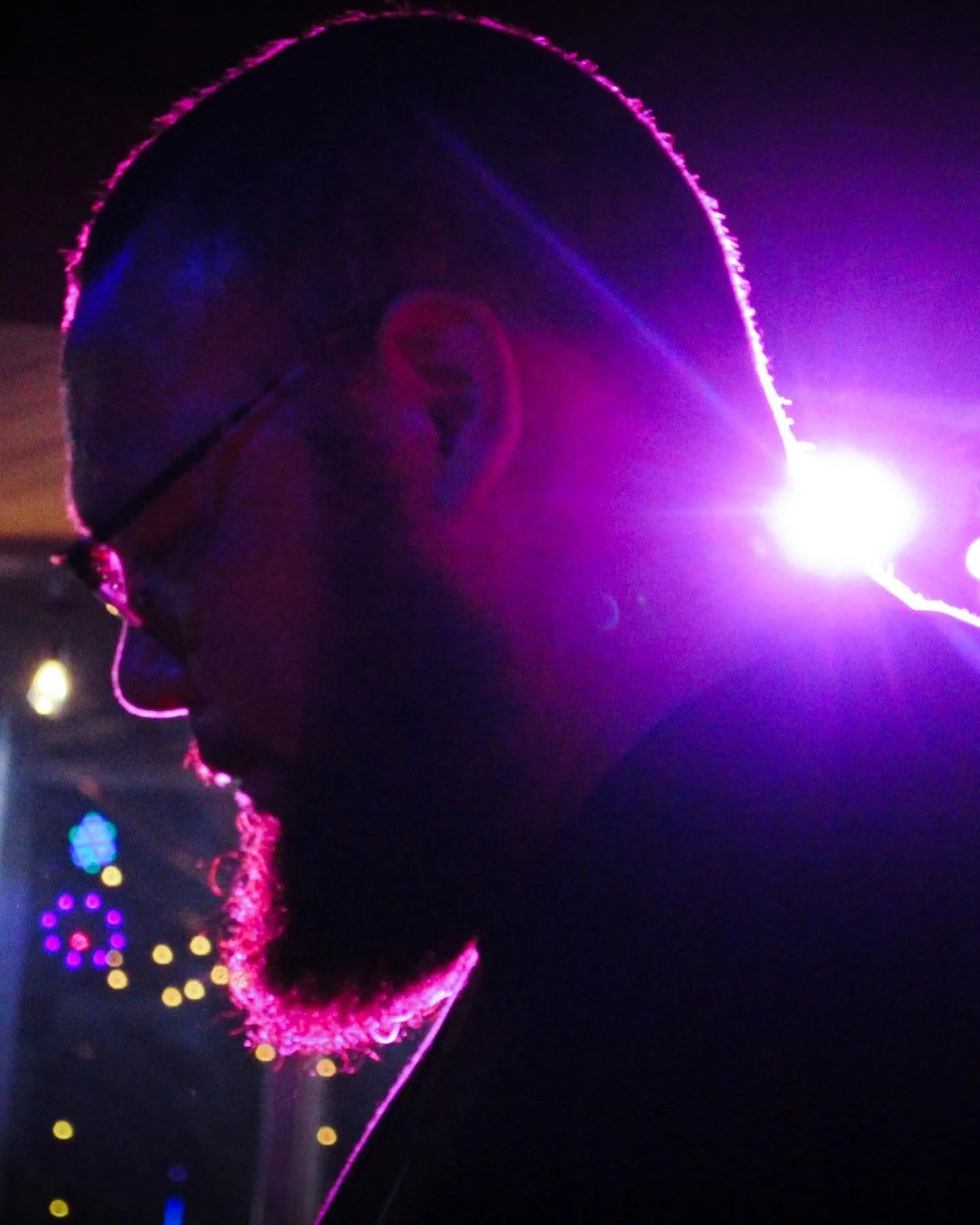 A person's profile silhouette illuminated by colorful lights, with pink outlines, purple glow, and bright spots of multicolored lights in the background.