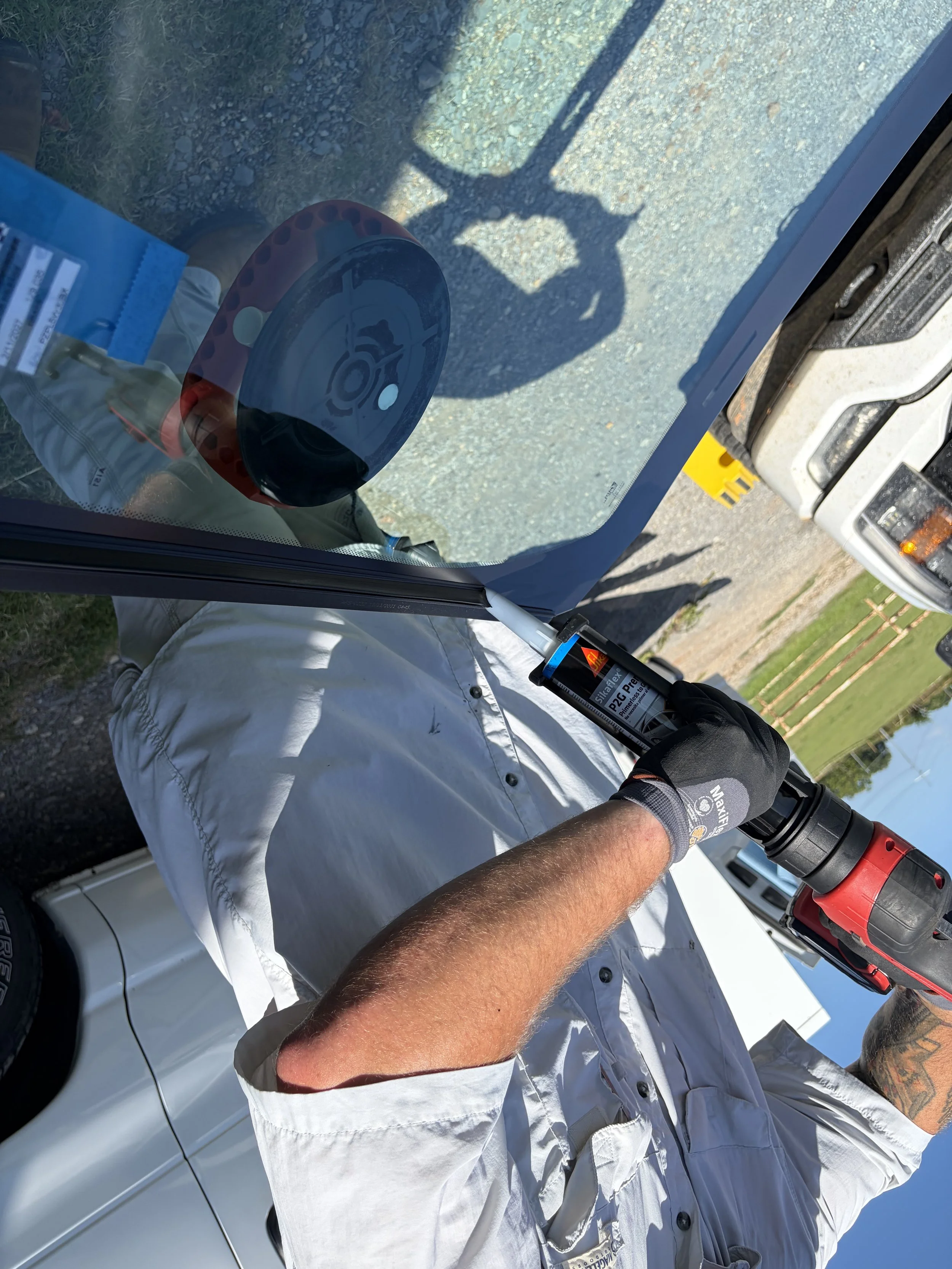 A technician is using a red caulk gun to apply urethane to a windshield just before installation.