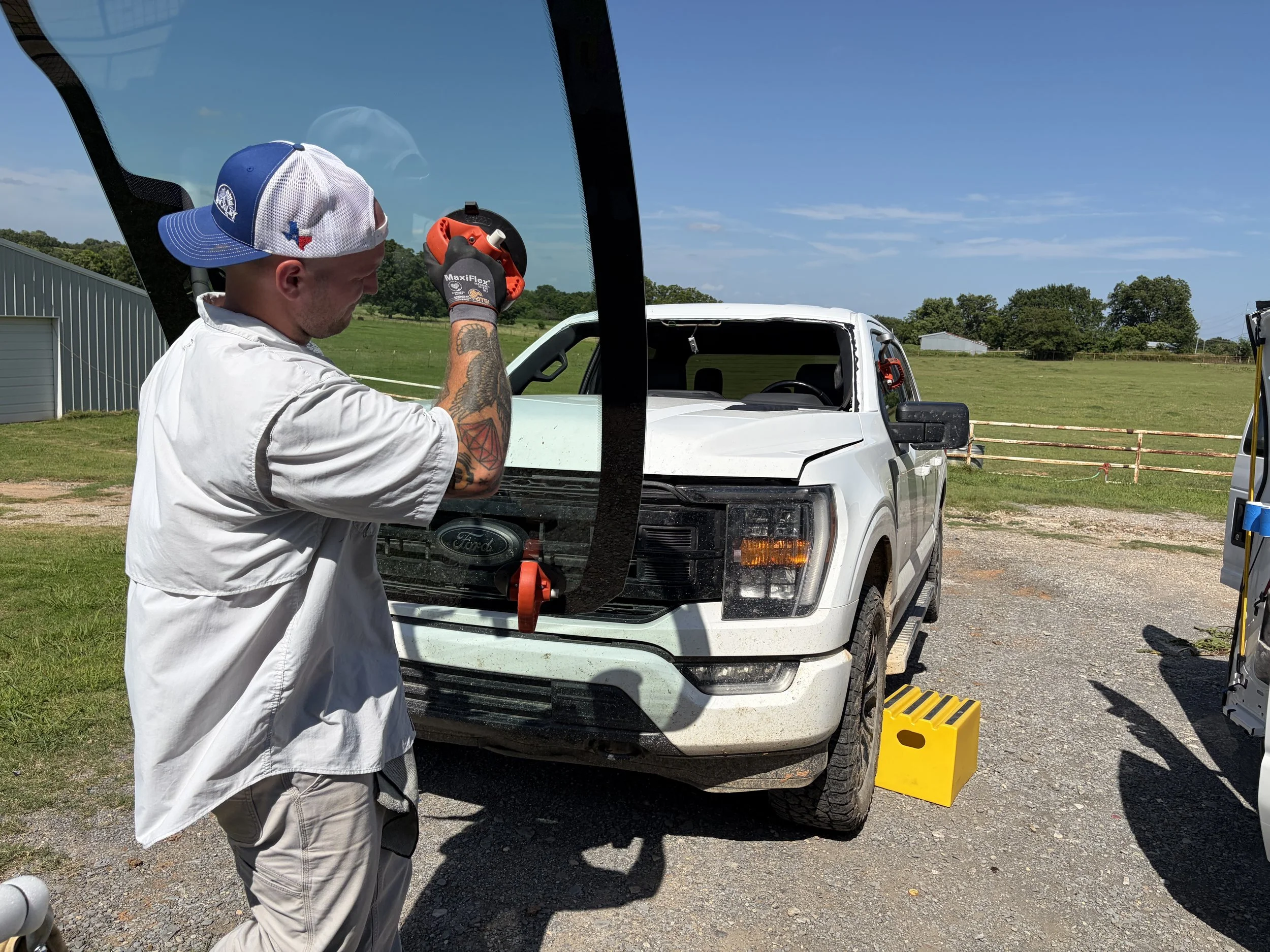 A technician carrying a windshield to a white Ford F150 to attach it on a one-man setting system prior to installation.