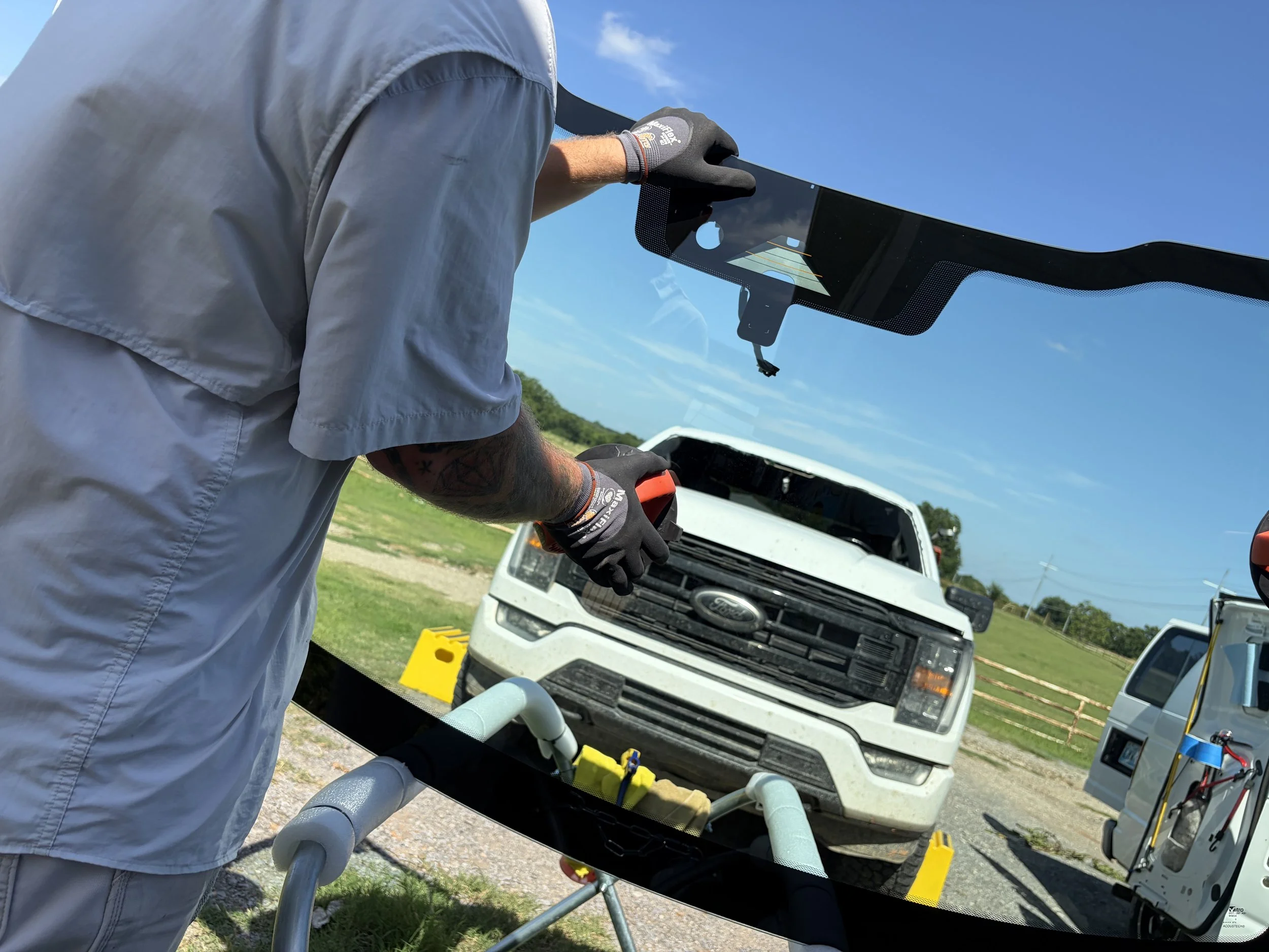 A windhsield with a suction cup being attached in front of a white Ford F150. The windshield of the Ford F150 has been removed and is being replaced.