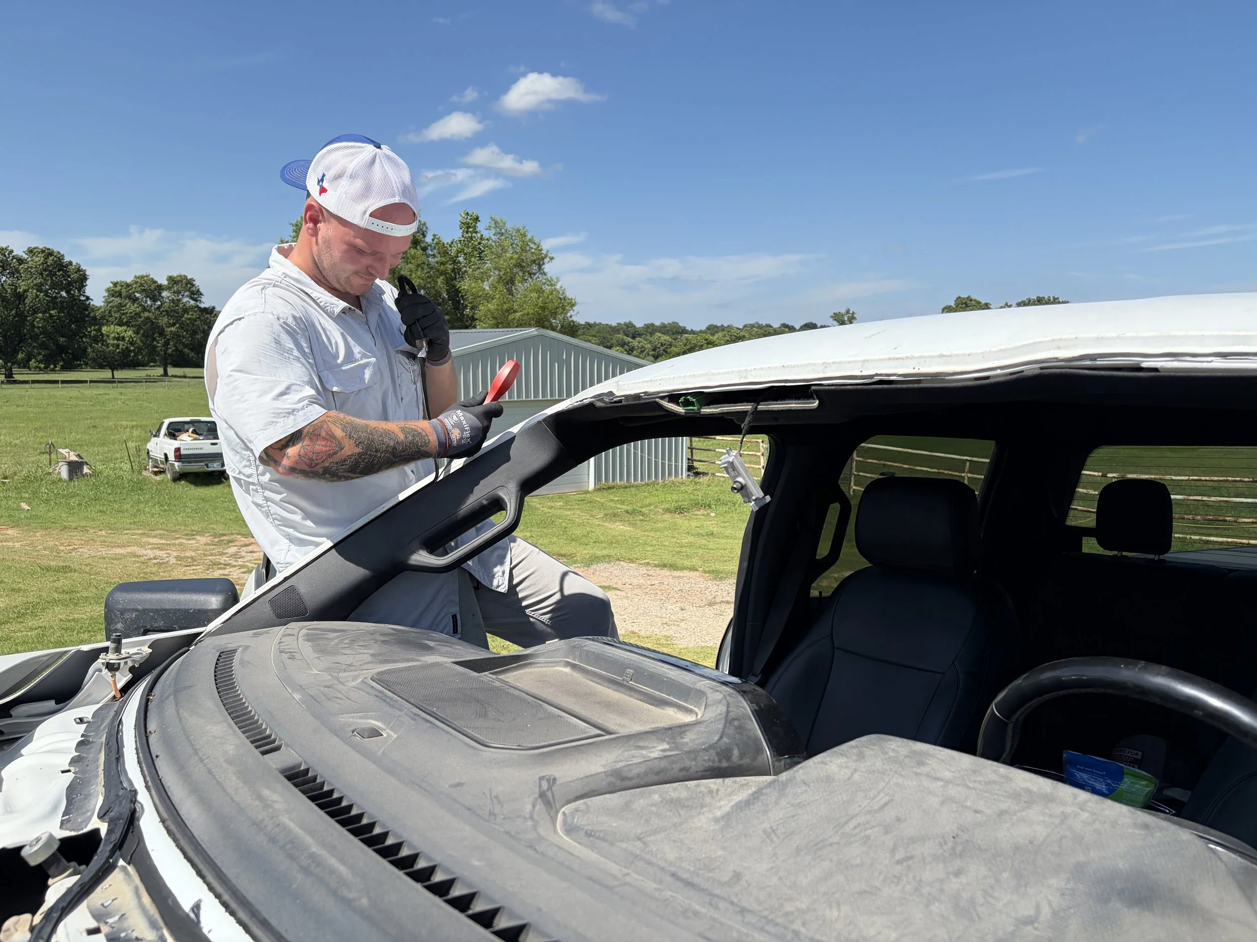 A technician is removing old urethane from the pinchweld of a white Ford F150 prior to installing the new windshield.