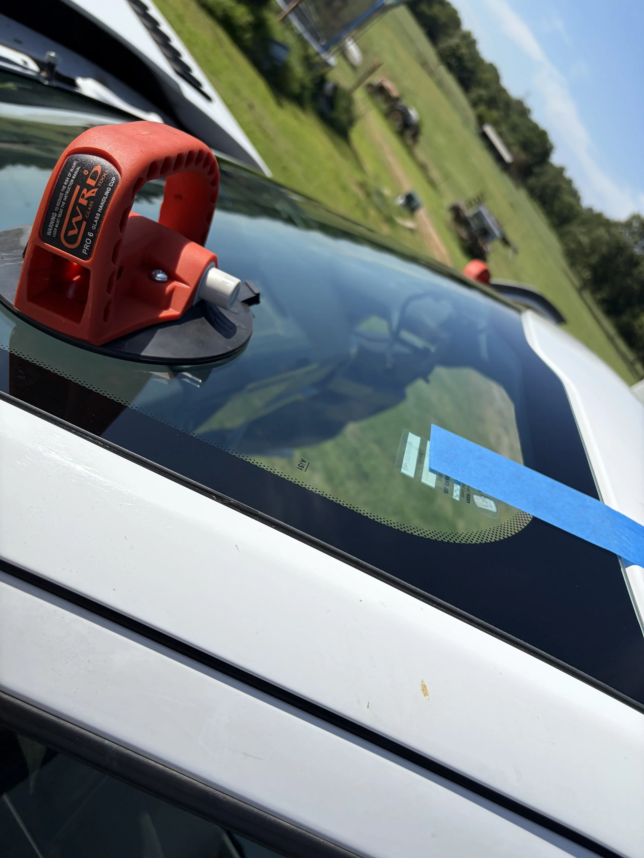 A close up of a suction cup on a recently replaced windshield being secured in place by blue tape.