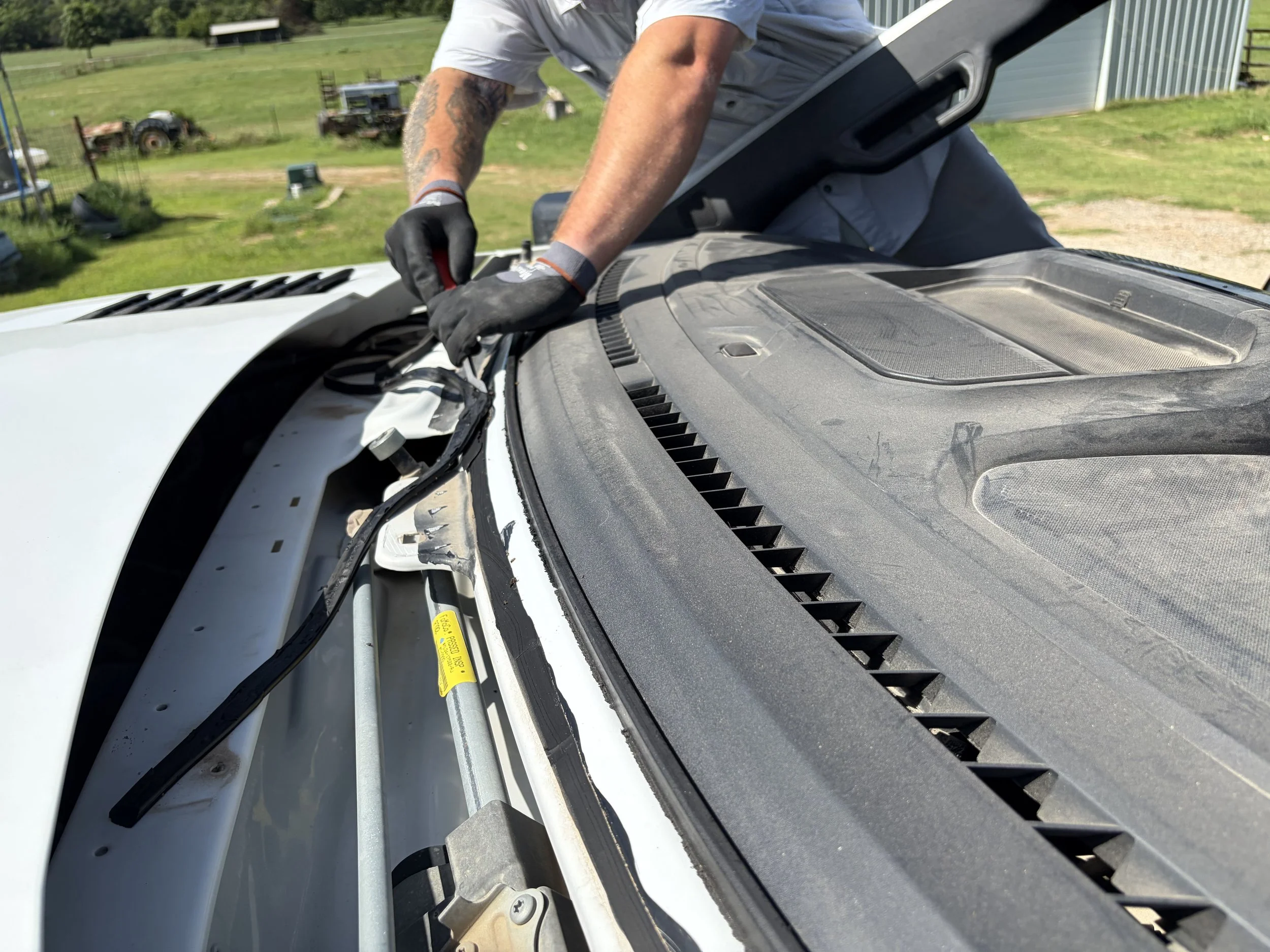 a technician is removing old urethane from the pinchweld of a white truck after the broken windshield has been removed.