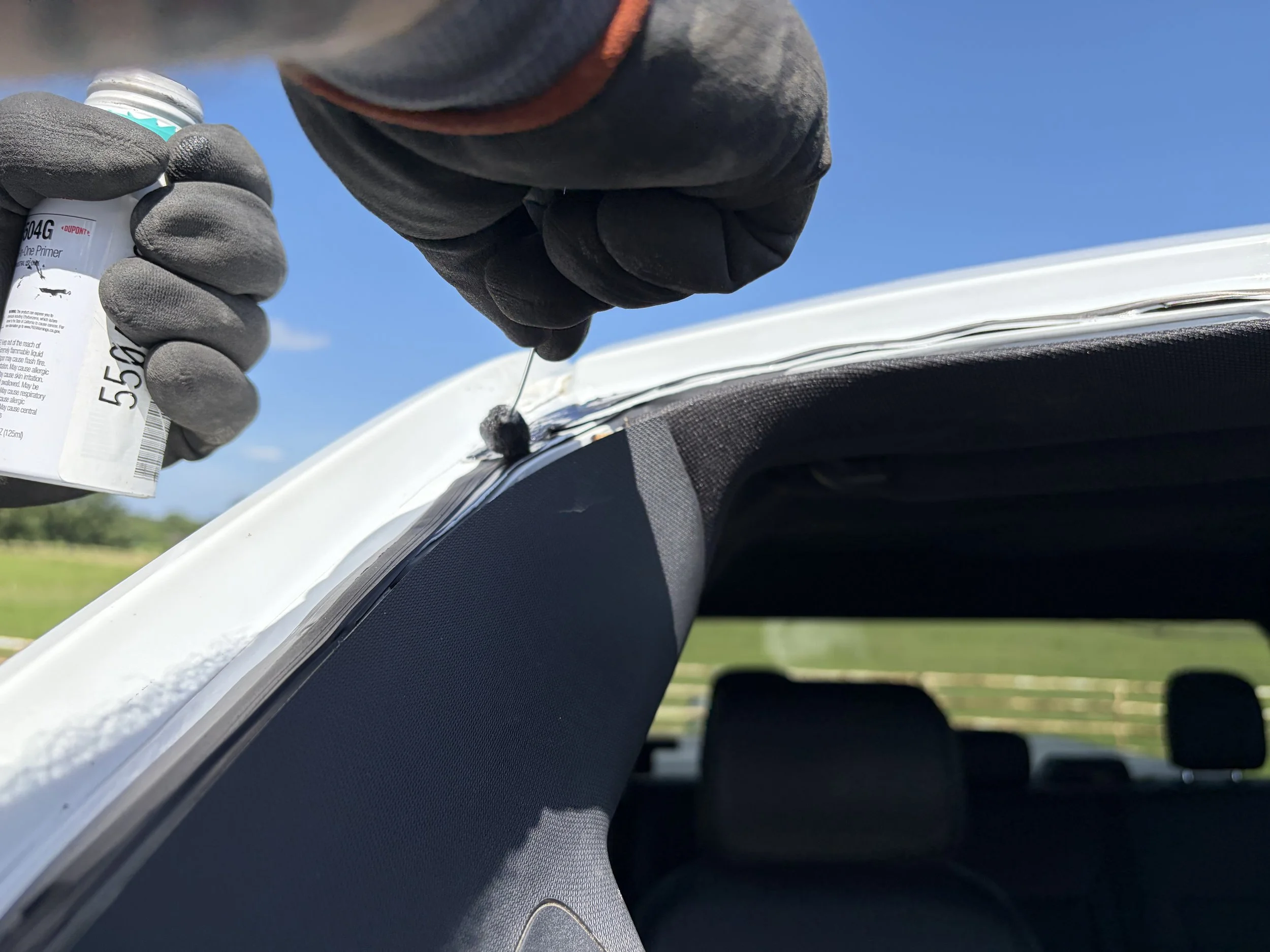 A close image of a technician applying primer to the pinchweld of a white vehicle.
