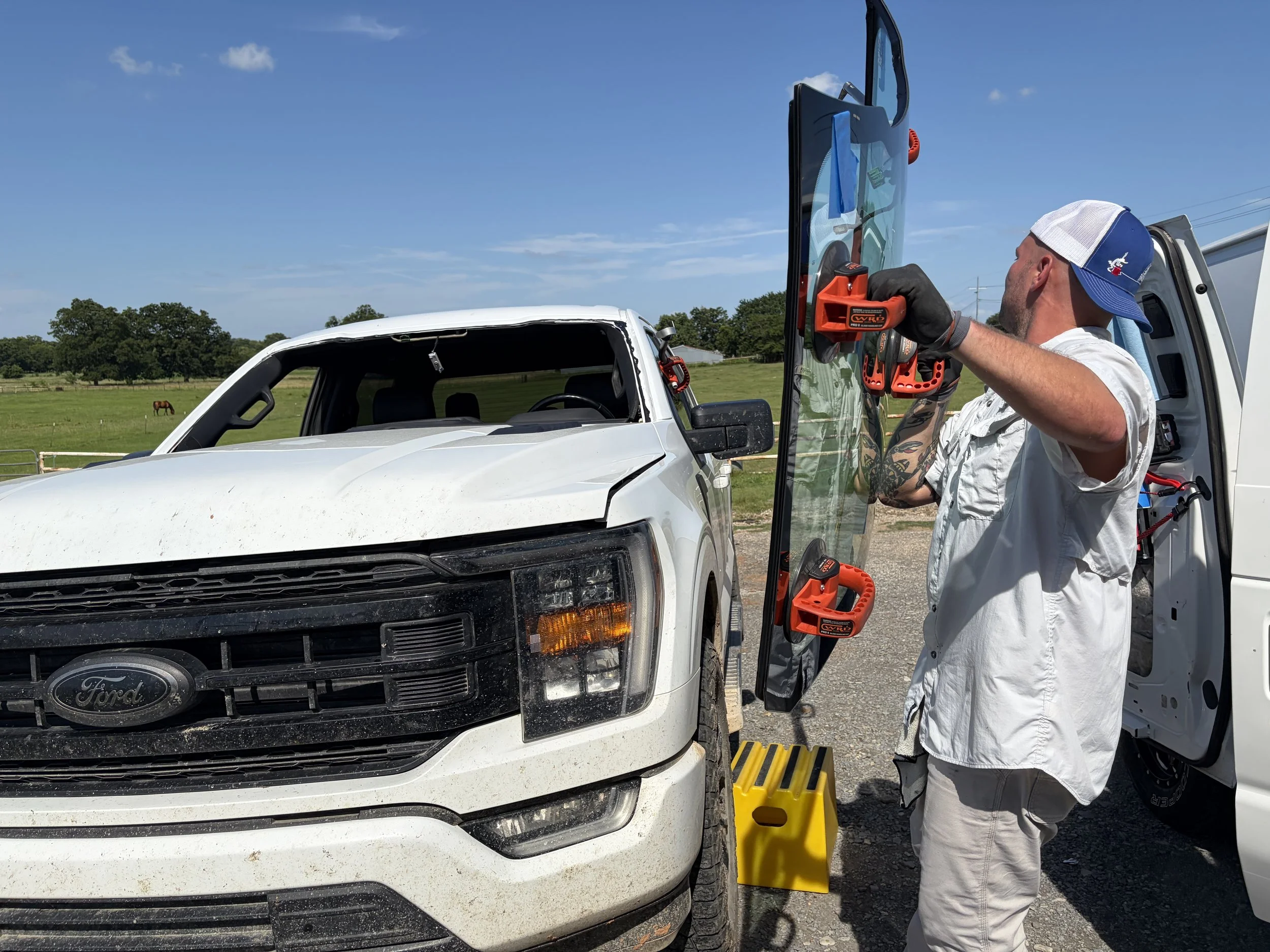 A technician installing a windshield on a white Ford F150. The technician is using a one man setting tool.