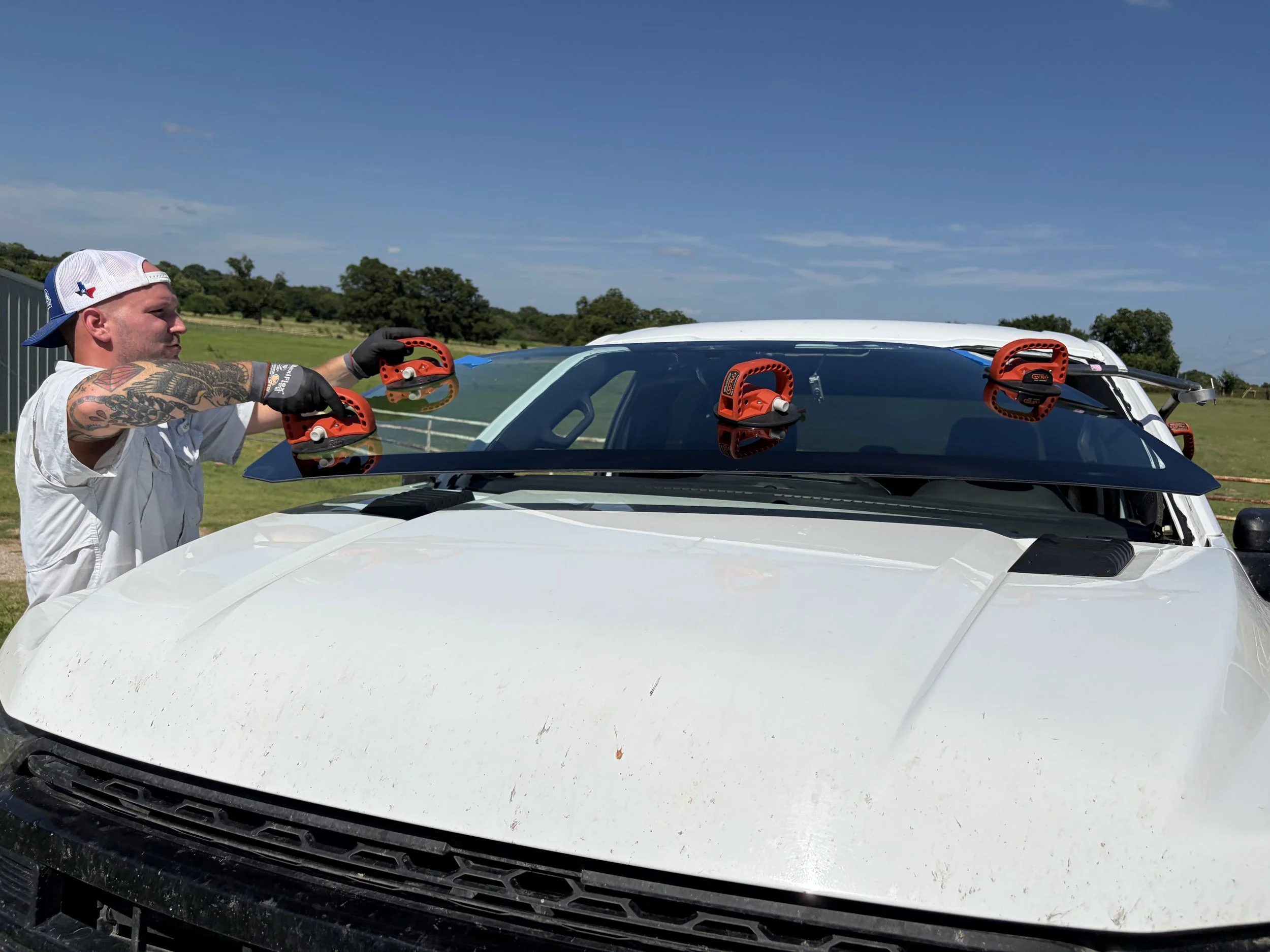 A technician replacing the windshield on a white Ford F150. The technician is using a one man set system to place the windshield into the truck properly.