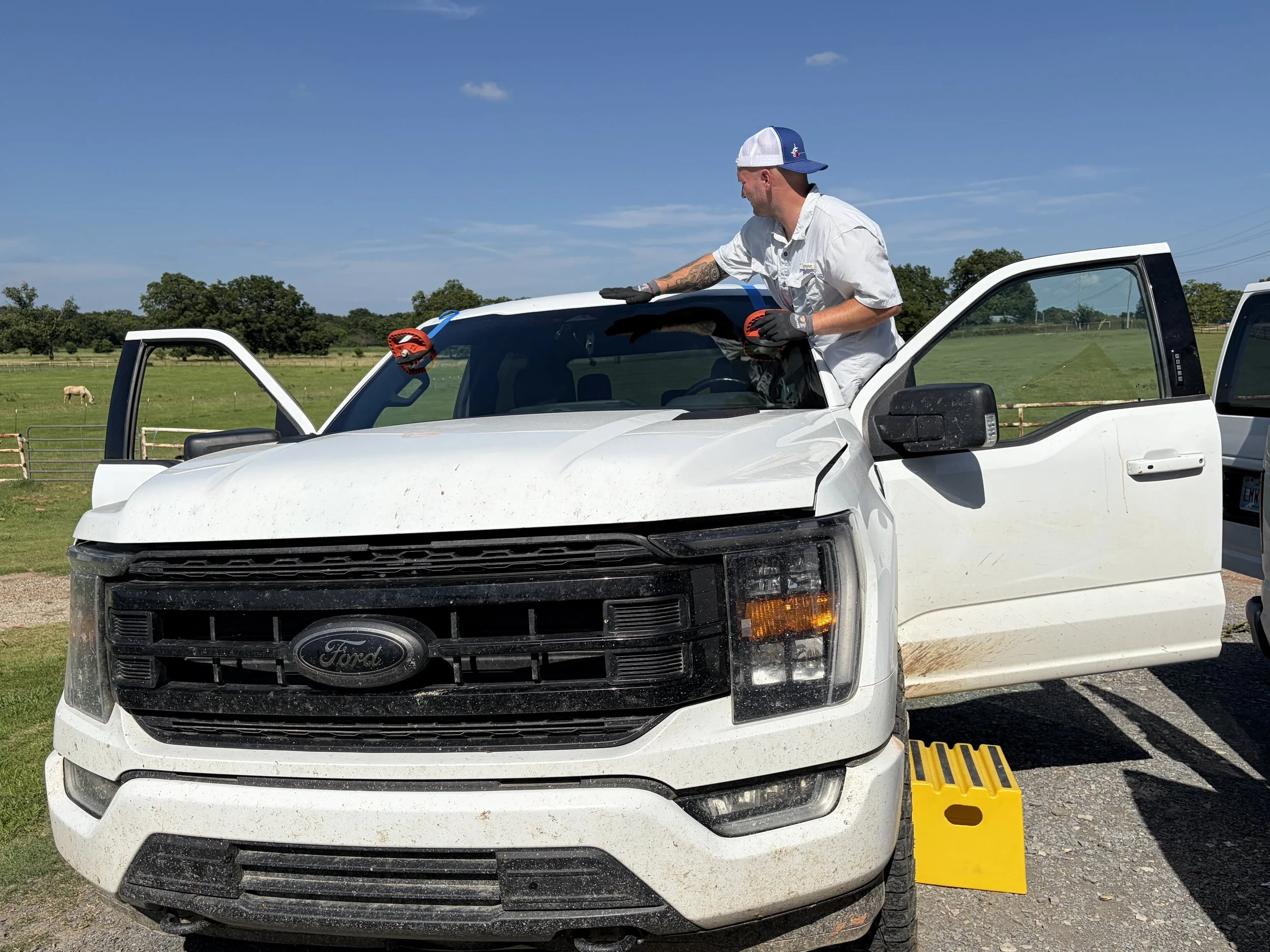 A whoite Ford F150 that has had a windshield just installed. The technician is ensuring that the windshield is properly decked.