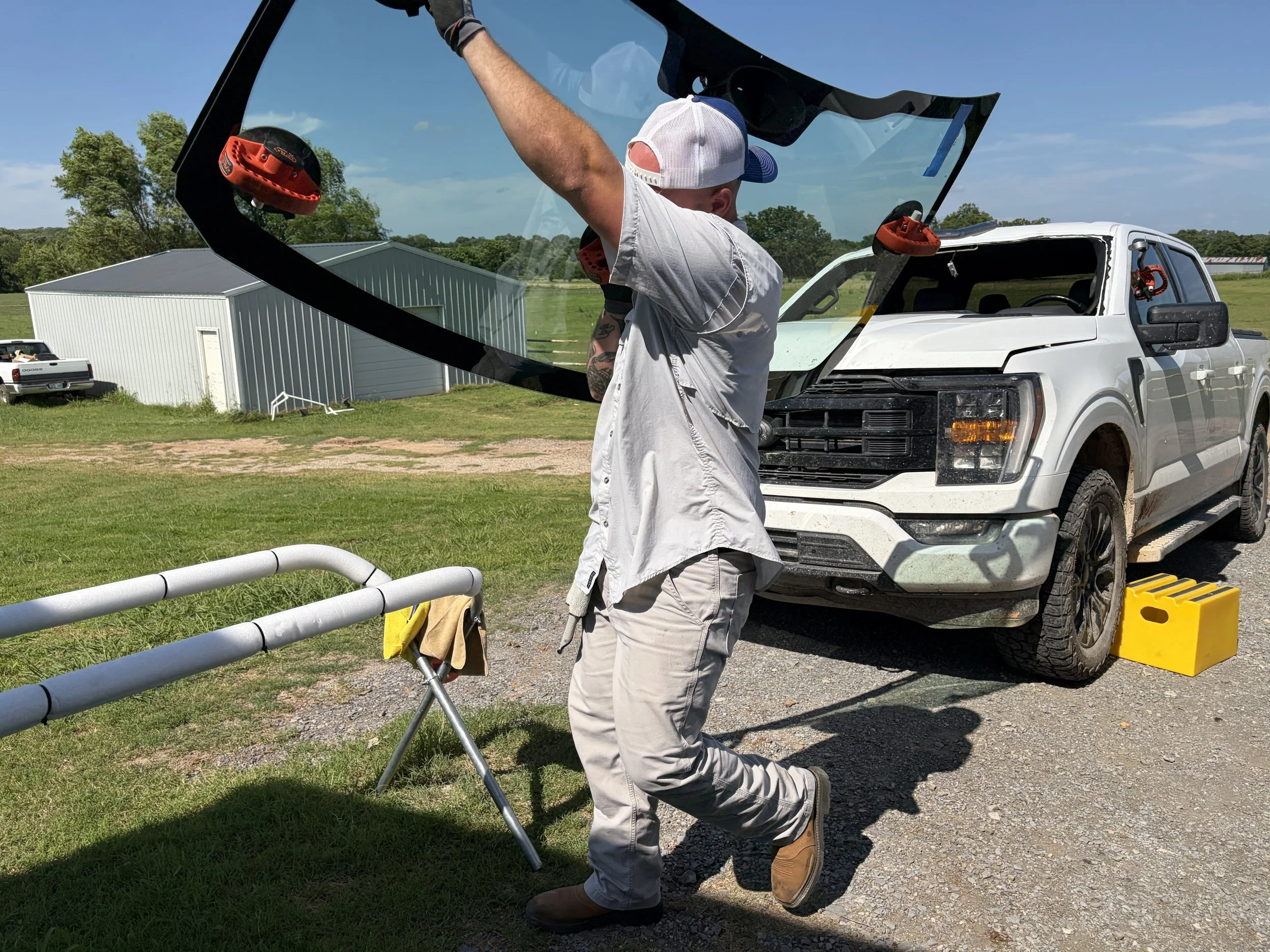 A technician is carrying the windshield over their shoulder with the use of suction cups. They are working on a white Ford F150.