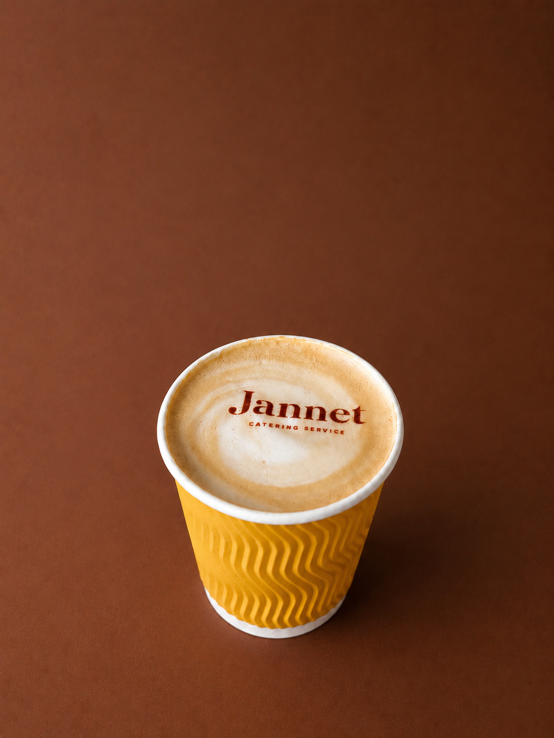 A paper coffee cup with a foam top displaying the logo 'Jannet Catering Service' on a brown background.