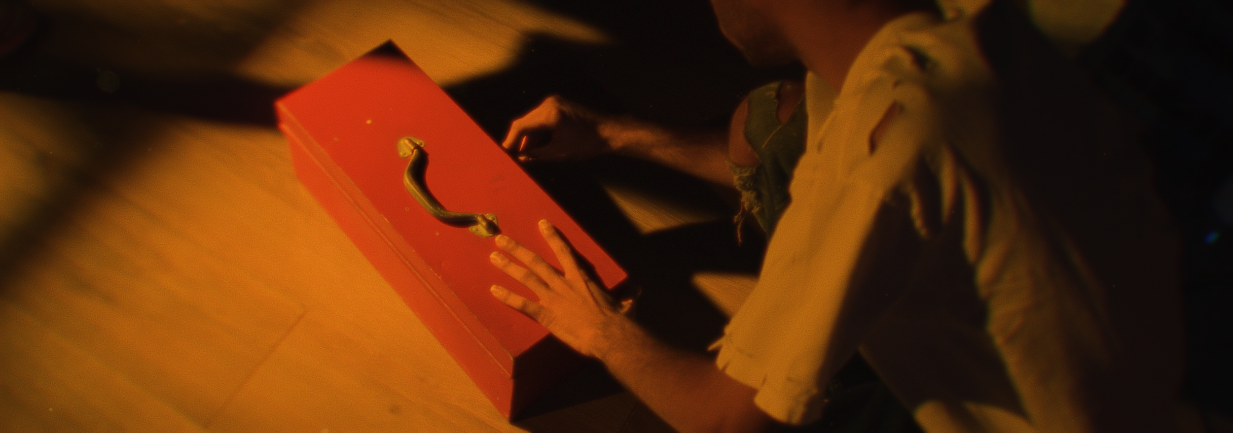 A person in a yellow shirt reaching for a red box with a handle.