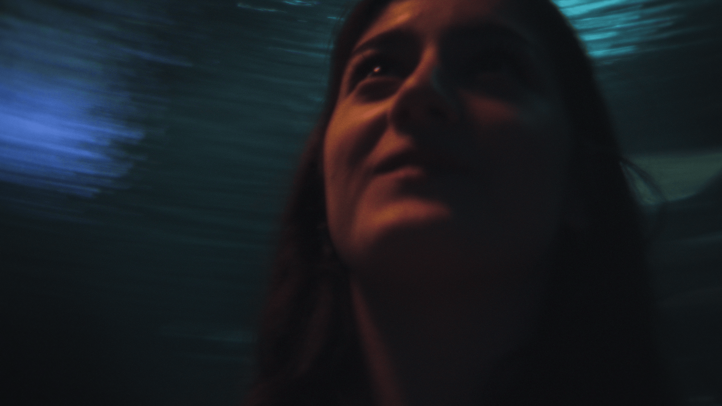 Close-up of a person's face underwater with a dark background and blue lighting.
