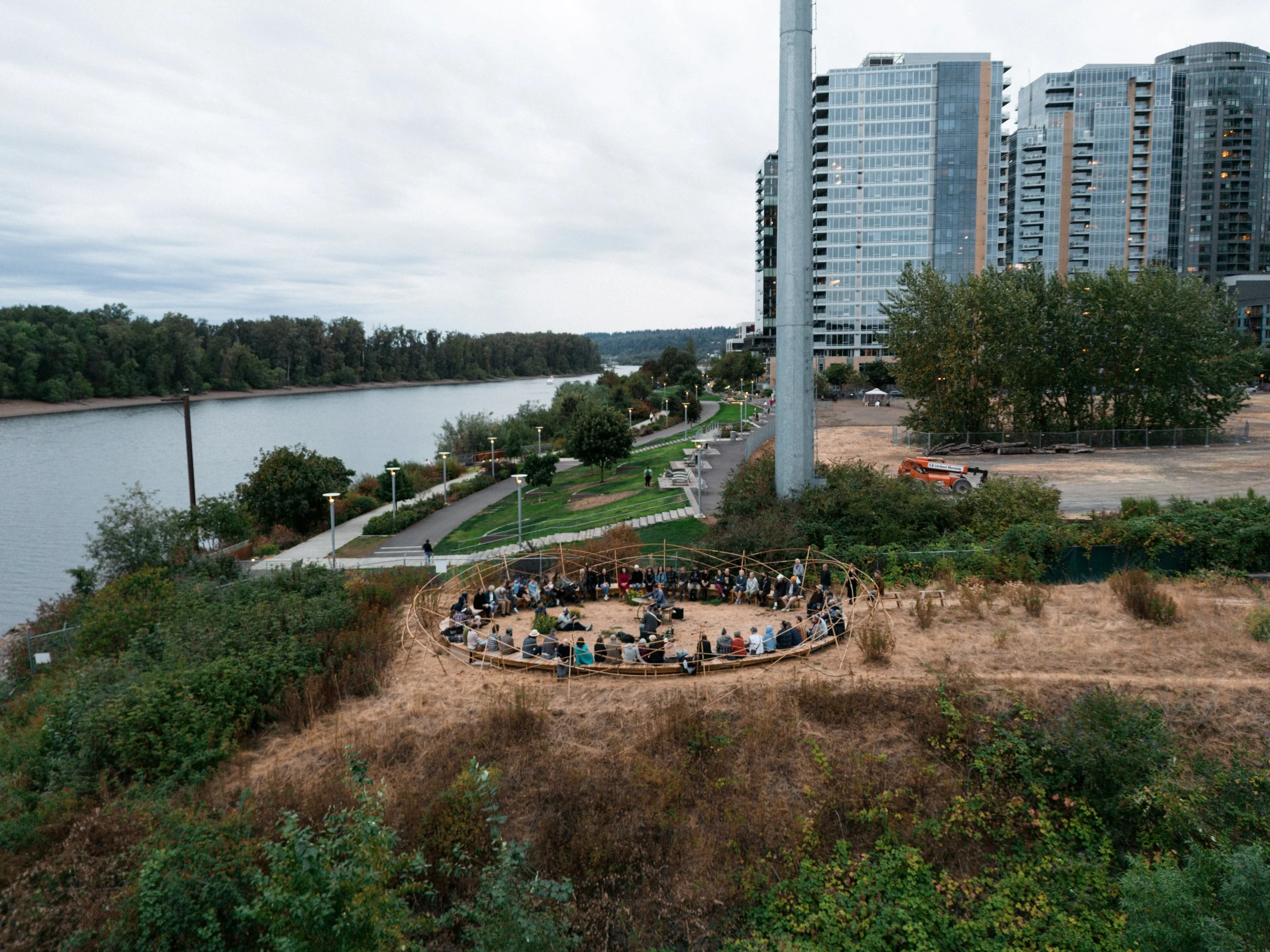 An aerial shot of the circular bench, filled with people.  In the background, the Willamette river and tall glass buildings.