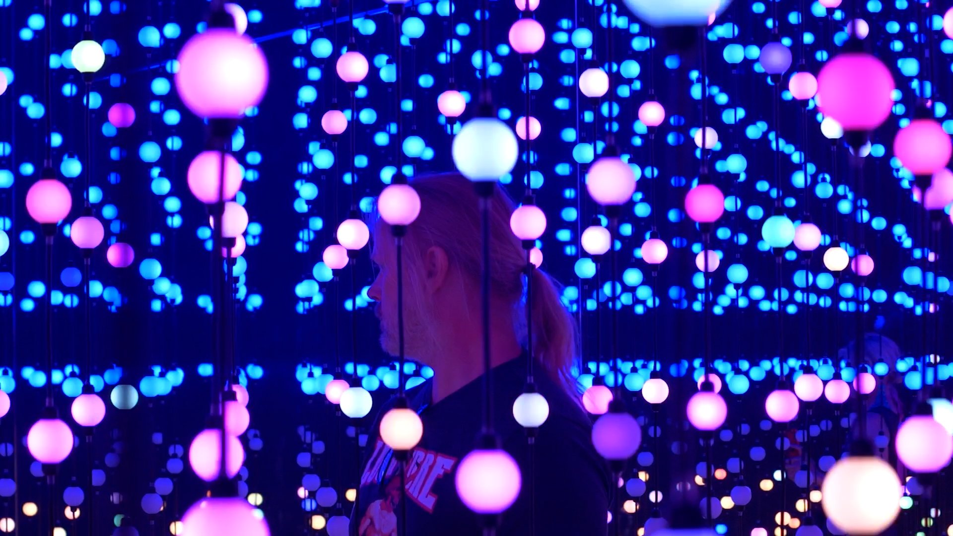 A man with long hair and beard stands in profile, surrounded by multicolored LED spheres Unknown Atmospheres by Seth Nehil and Parallel Studio at Hopscotch Gallery
