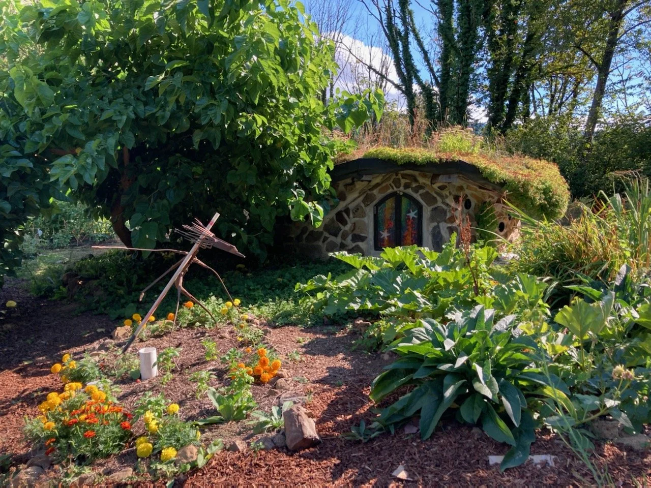 A low stone circular structure with a living roof, surrounded by gardens.