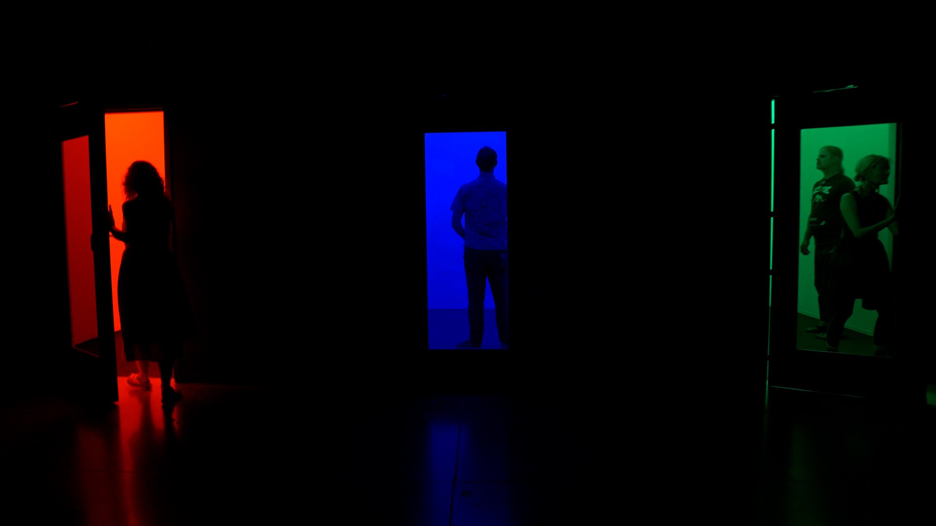 Three doorways, glowing in an otherwise dark space - red, blue and green.  Figures stand as silhouettes in each door.
